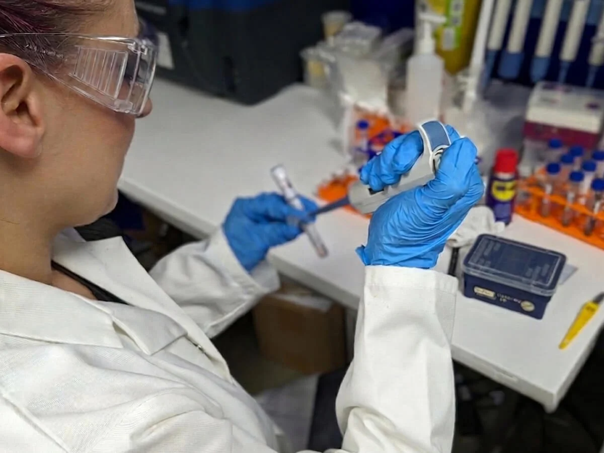 A scientist wearing safety glasses and blue gloves working in a laboratory.
