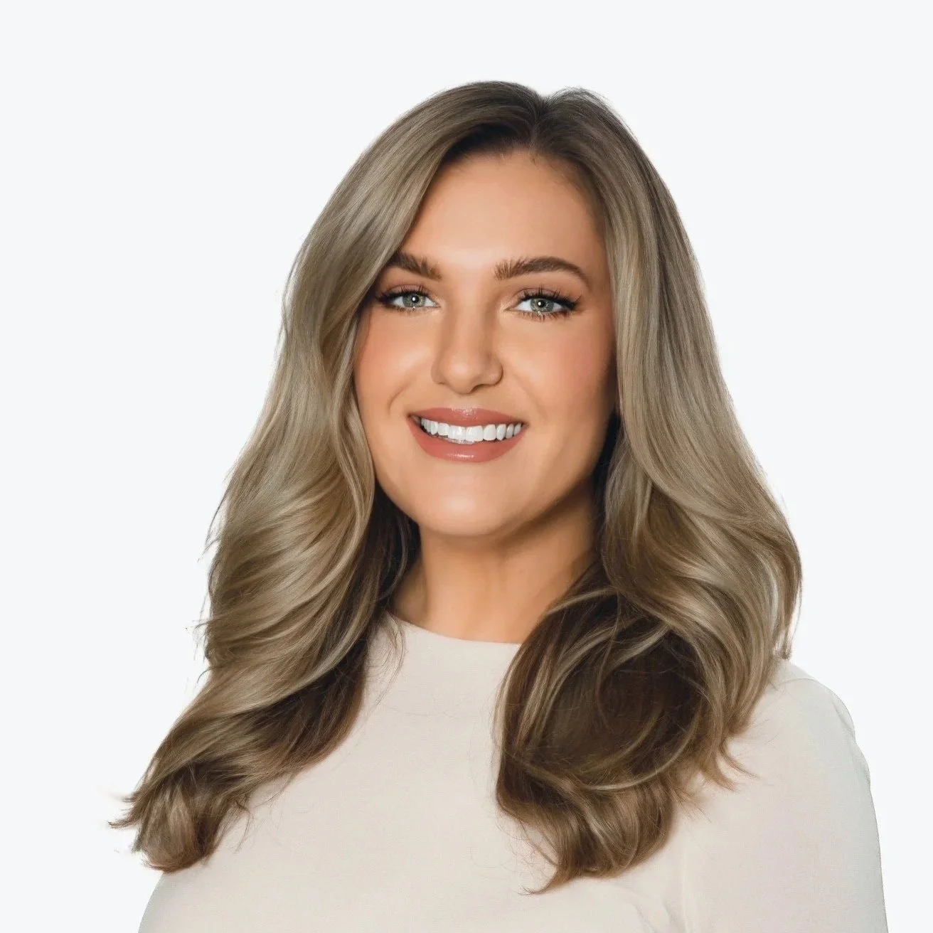Portrait of a smiling woman with long, wavy blonde hair, wearing a white top, against a plain light background.