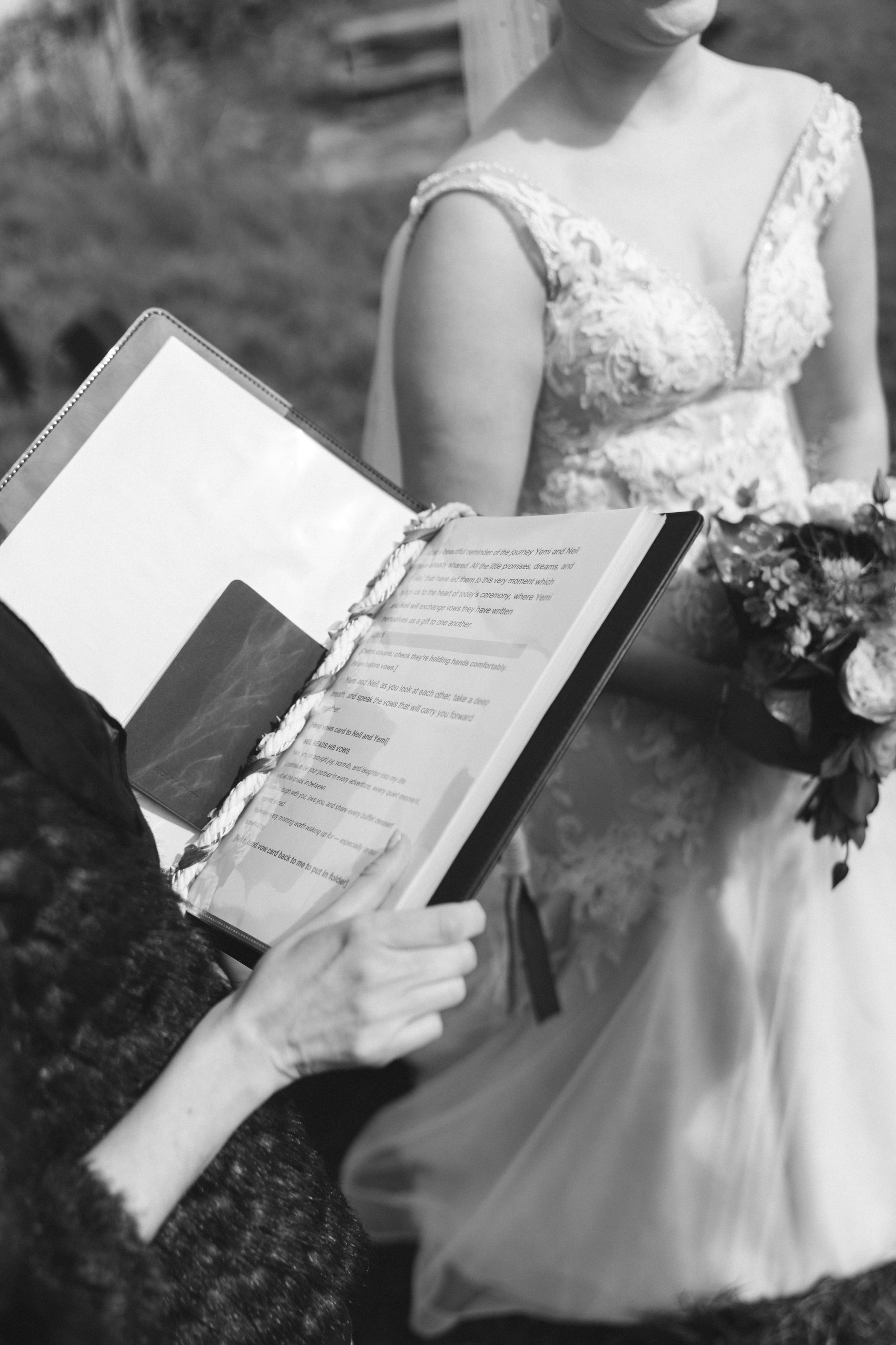 A person holding an open book or possibly a script, with another person in a wedding dress visible in the background.