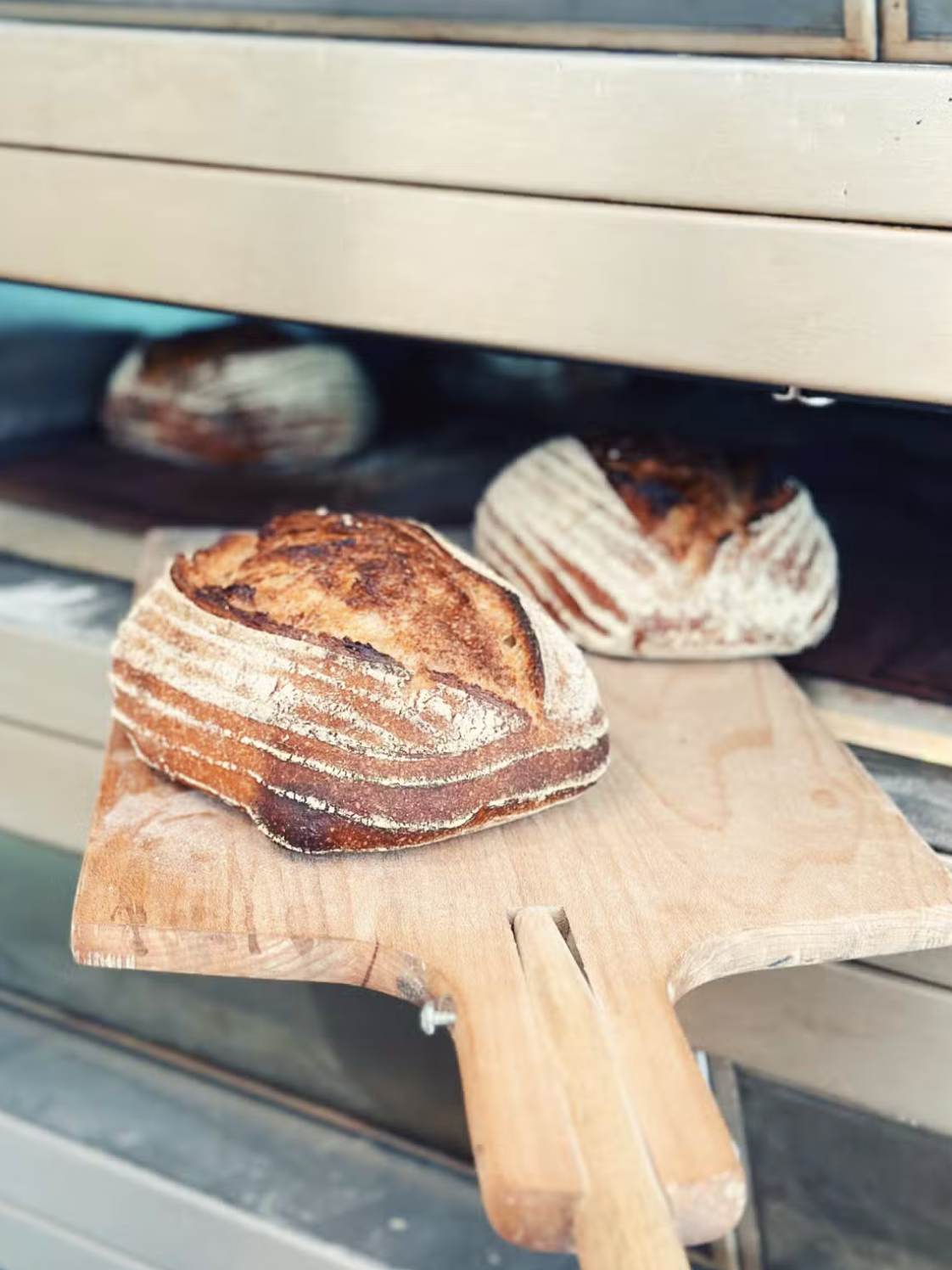 Brood met een krokante, goudbruine korst op een houten snijplank, bakoven op de achtergrond.