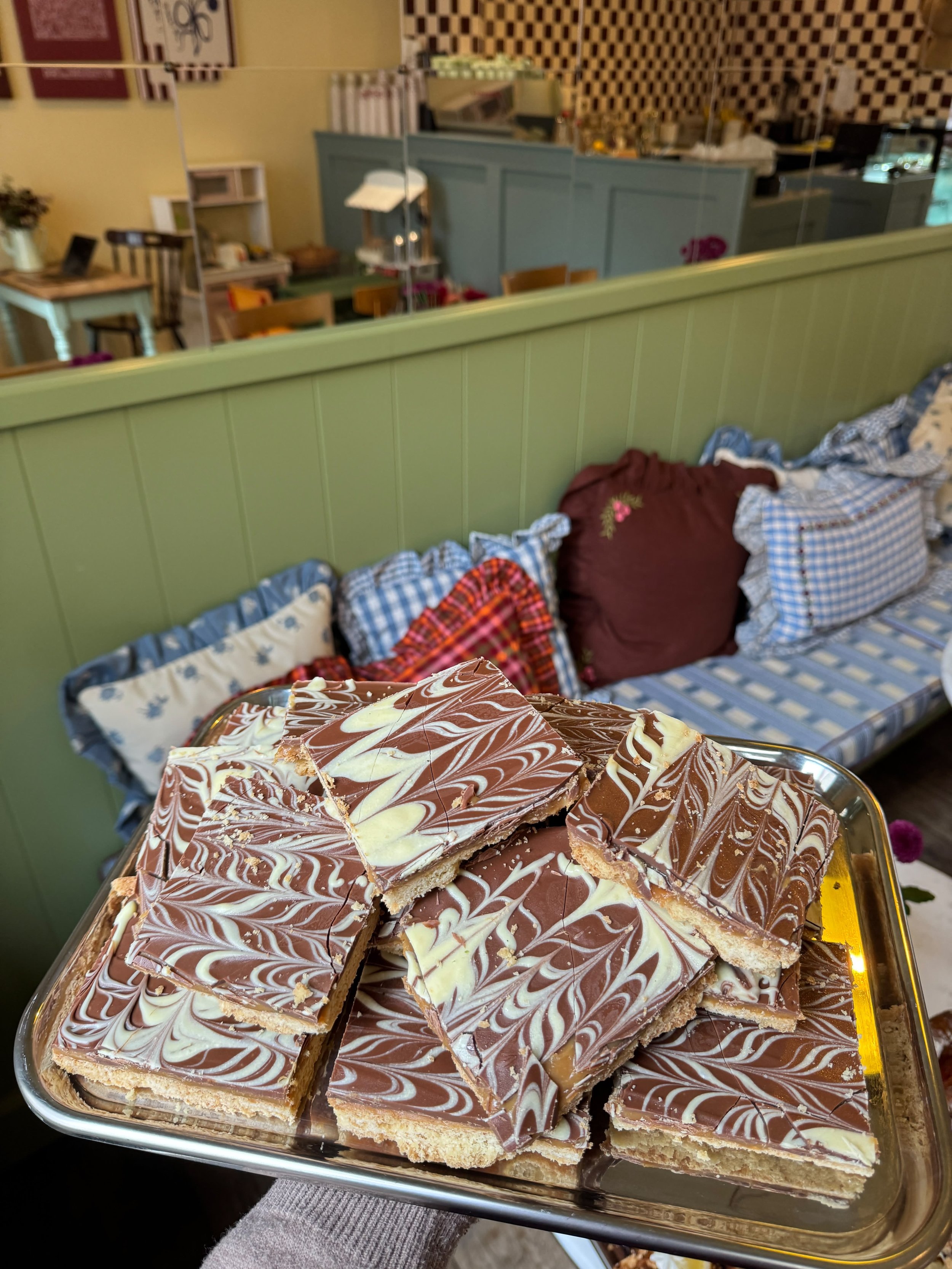 Een dienblad met stukjes chocolade-karamel lakelijne op een tafel in een foodcafé of restaurant, met een achtergrond van verschillende meubelen en decoraties.