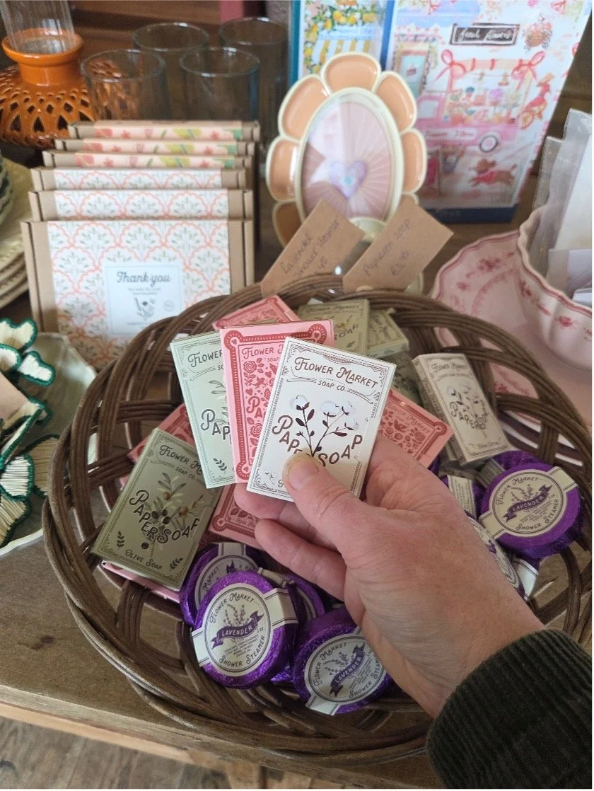 Een mand met verschillende zeepjes en handwaren, onder andere lavendelgeur shower soap en papieren kaarten met bloemmotieven.