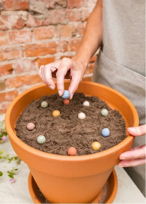 Persoon die gekleurde chocolade-eitjes in pot met aarde plant, tegen bakstenen muur