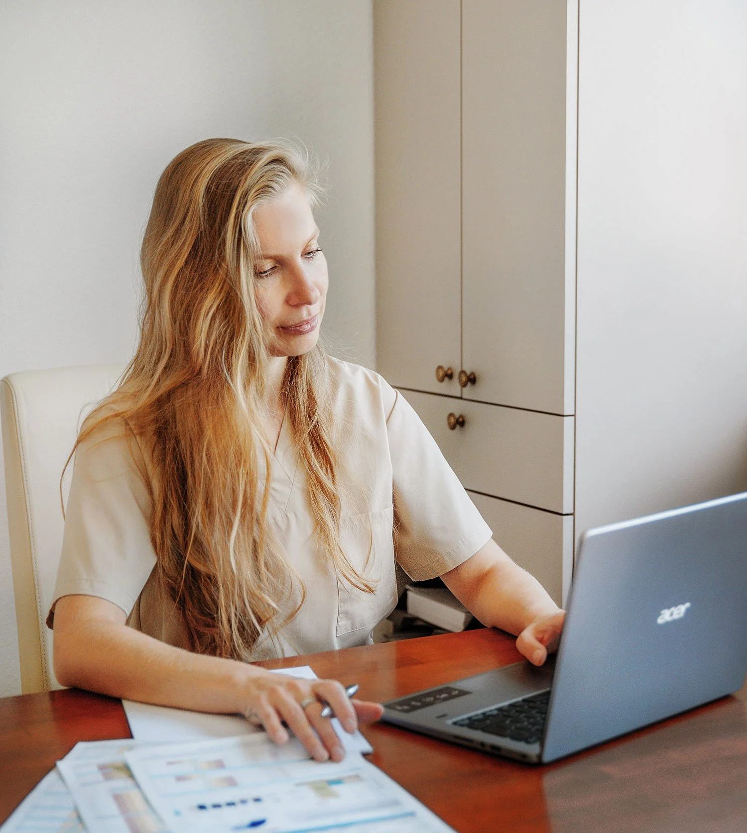 Frau arbeitet am Laptop in einem Büro, mit Unterlagen und Papieren auf dem Tisch.
