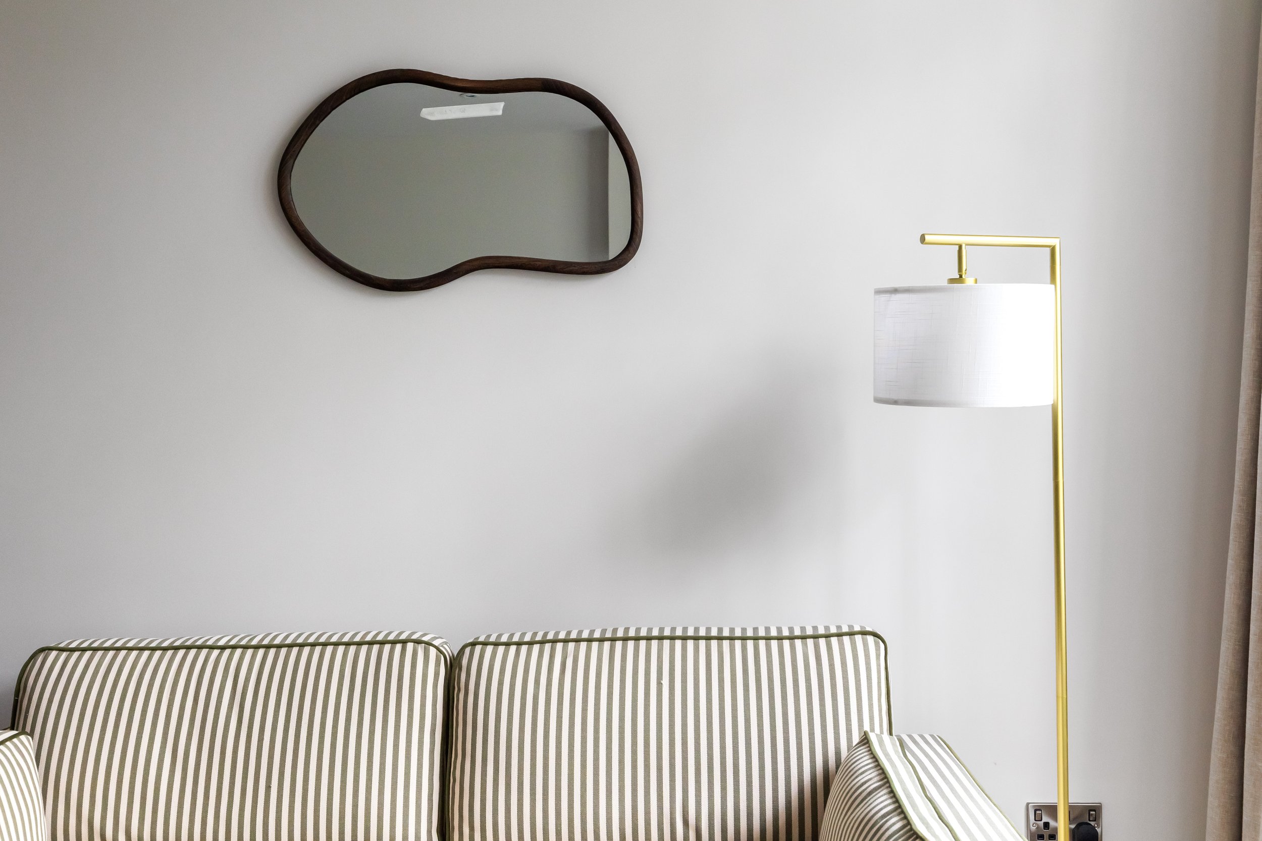 A striped sofa in front of a white wall with a mirror and a yellow floor lamp.