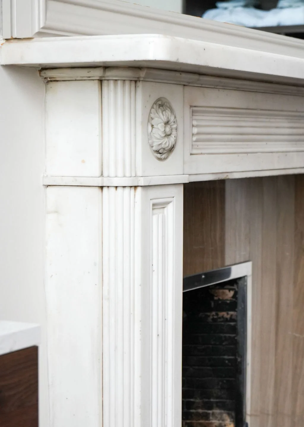 Close-up of a white, decorative mantel with carved floral details and vertical fluted accents.