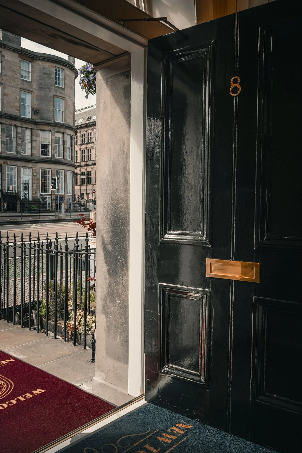 Open black door with gold mail slot, view of city street and historic buildings outside.