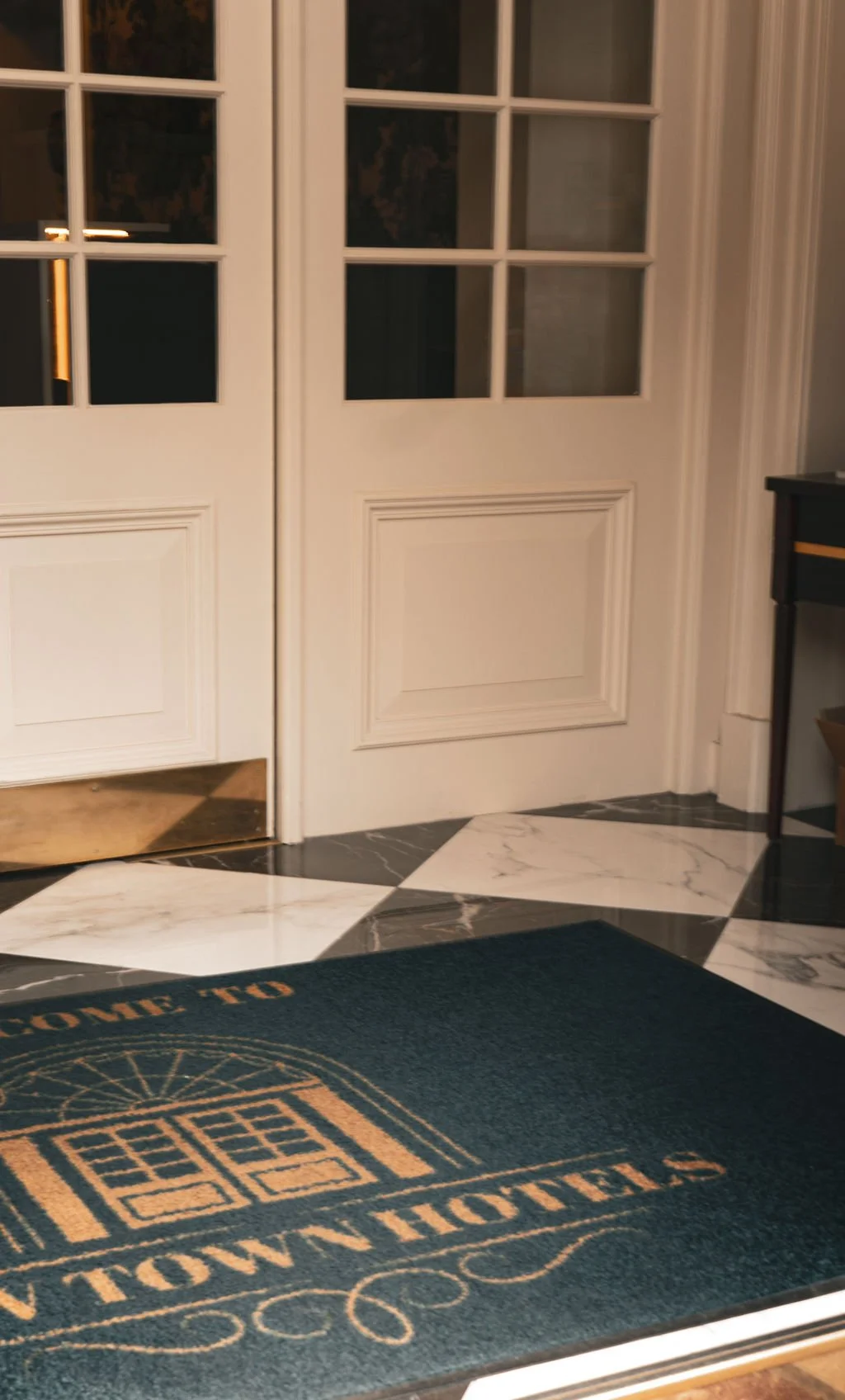 Entryway with white double doors with glass panes, marble tile floor, and a dark green welcome mat that says "Home Sweet Home."
