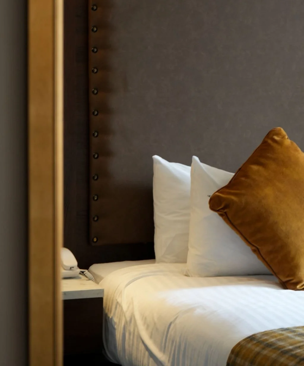 View of a neatly made bed with white pillows and bedding, framed by a partially opened door in a modern hotel room.
