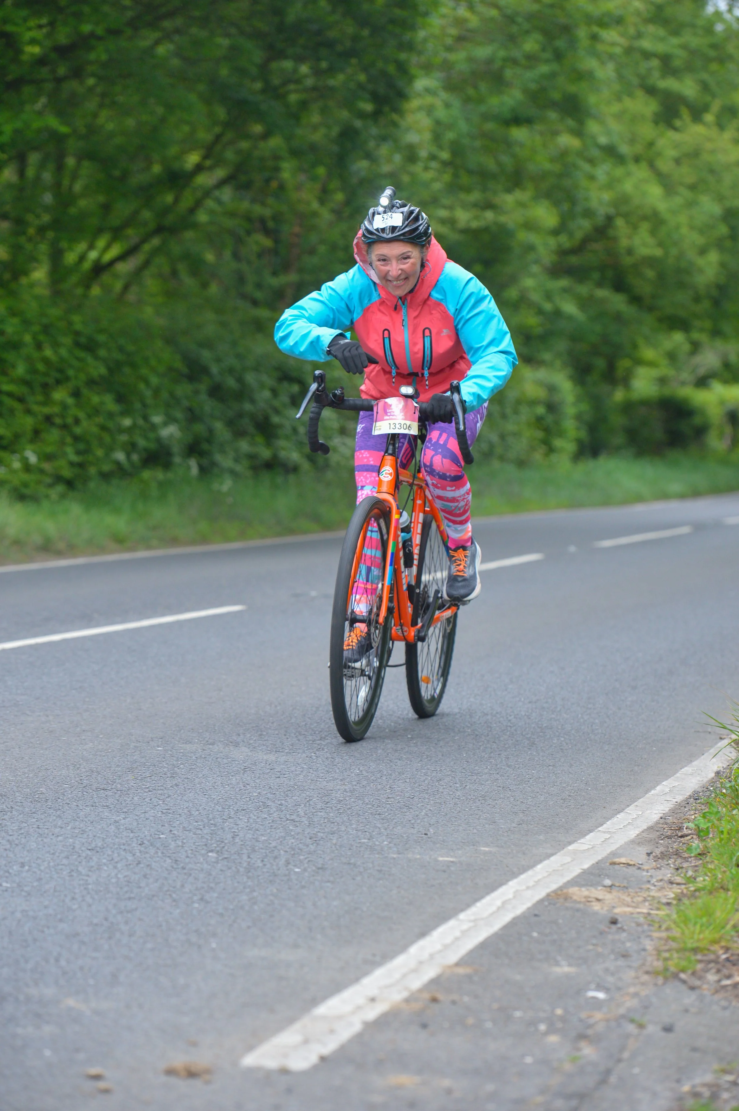 A woman riding a bicycle on a paved road surrounded by green trees and bushes.