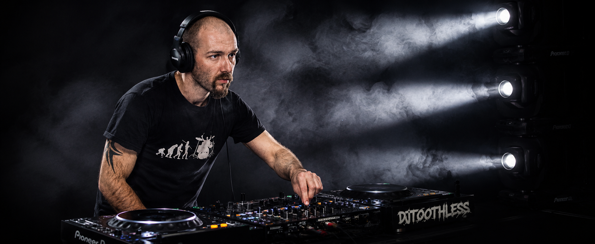 A man DJing with headphones on, operating a DJ mixer and turntables, with fog and stage lights in the background