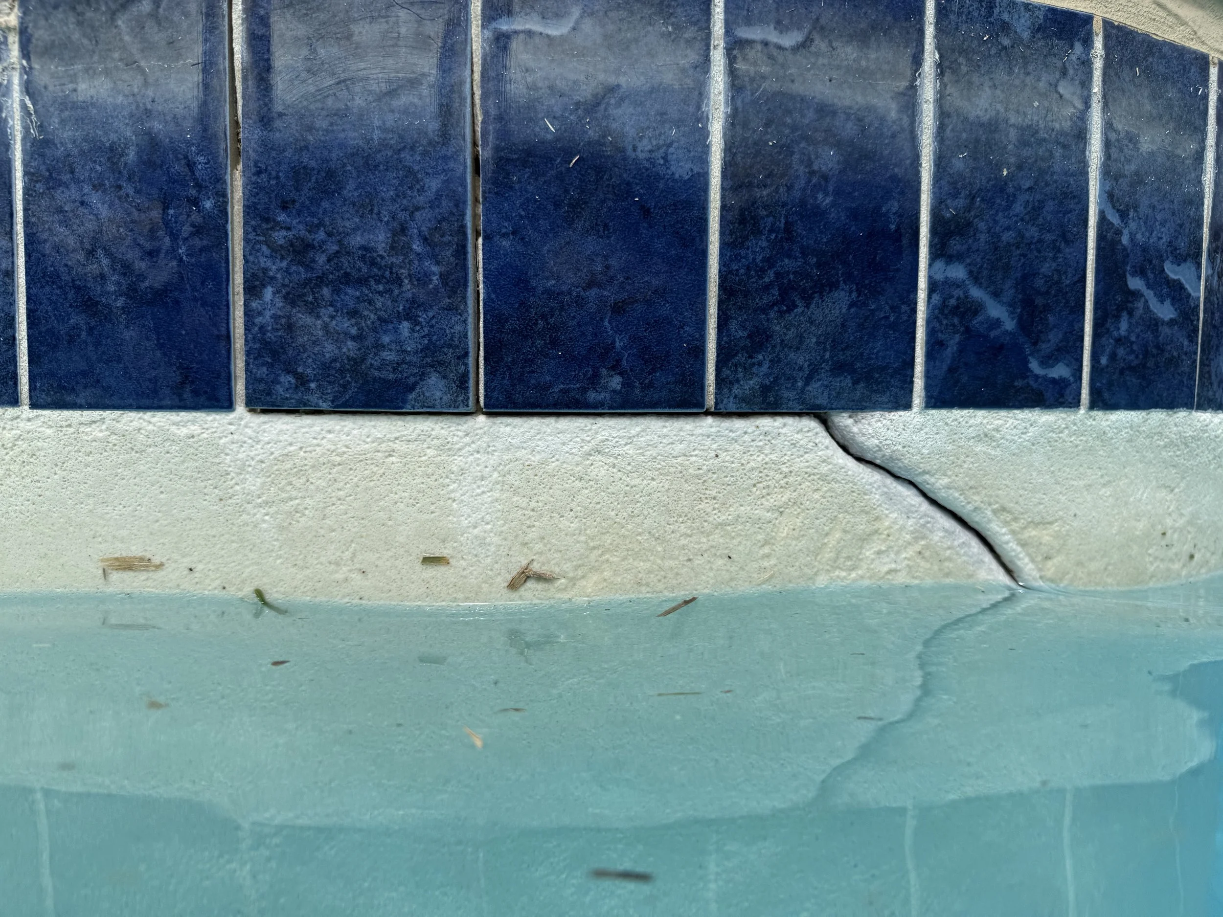 Close-up image of several blue ceramic tiles arranged horizontally on a wall, with some dirt and a crack visible on the surface.