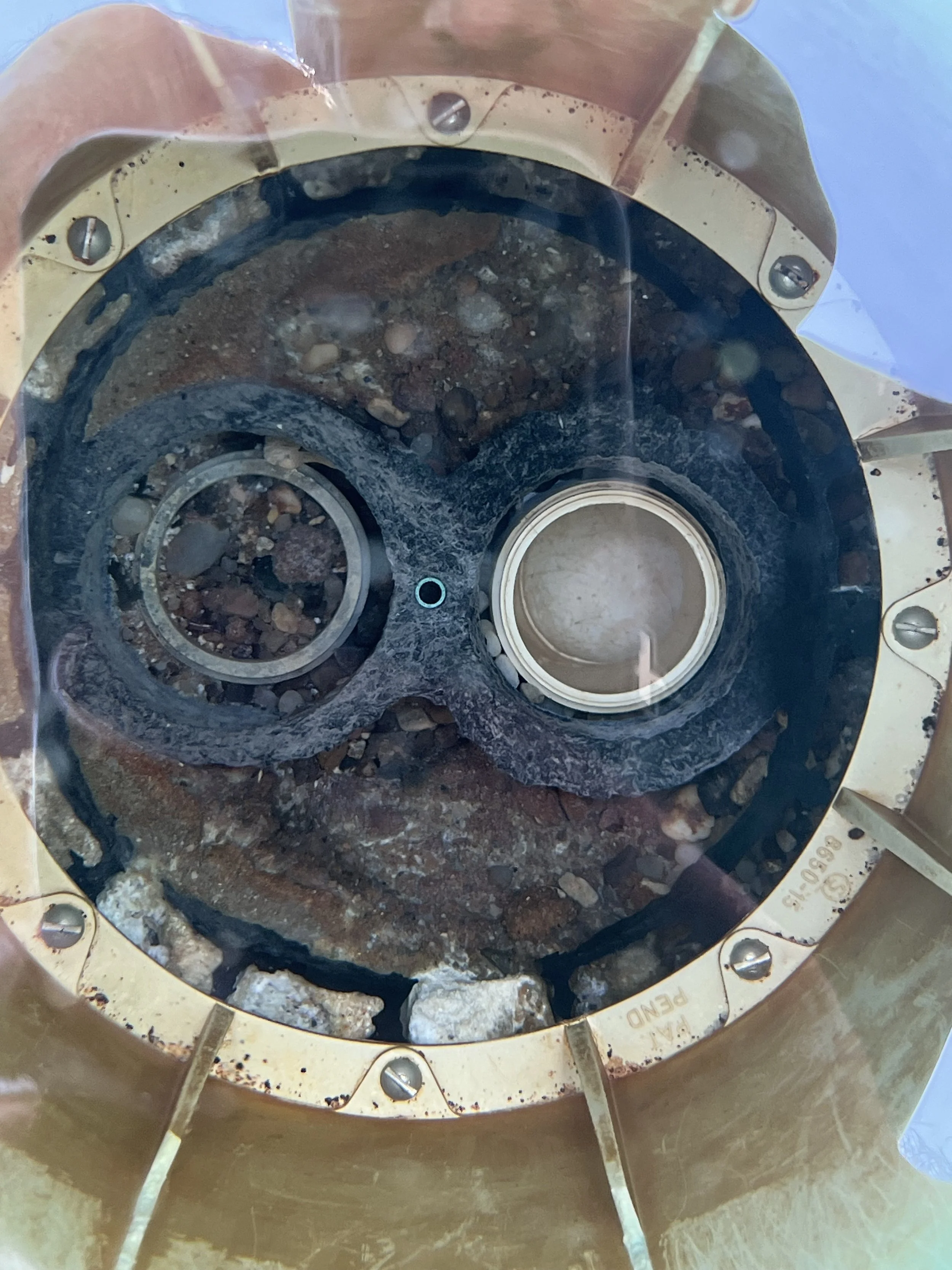 Close-up of a mechanical part inside a metal casing, with corroded components, bolts, and visible dirt or debris.