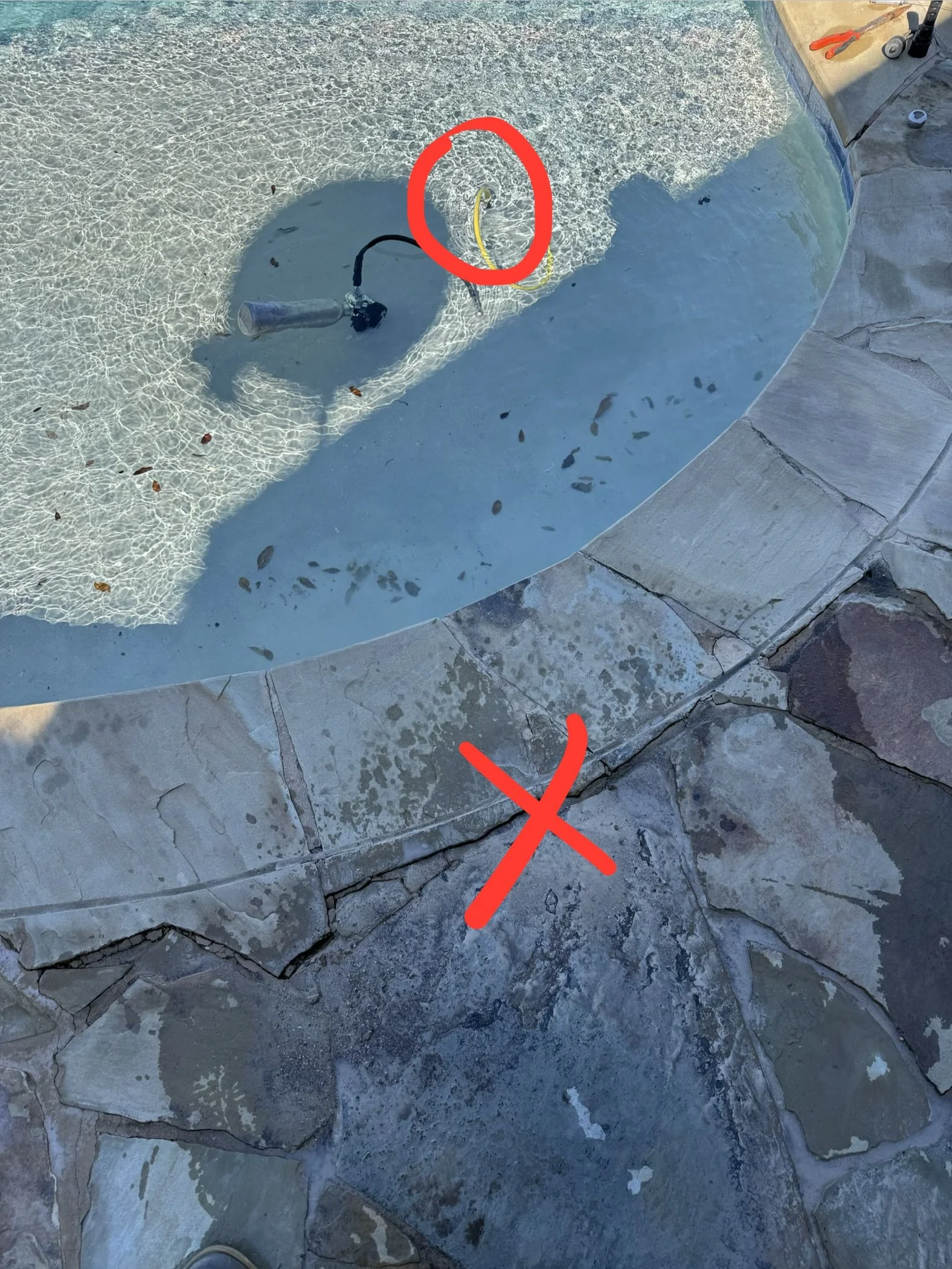 In-ground swimming pool with exposed plumbing, yellow hose, and construction tools on the deck, marked with red circles and arrow for highlight.
