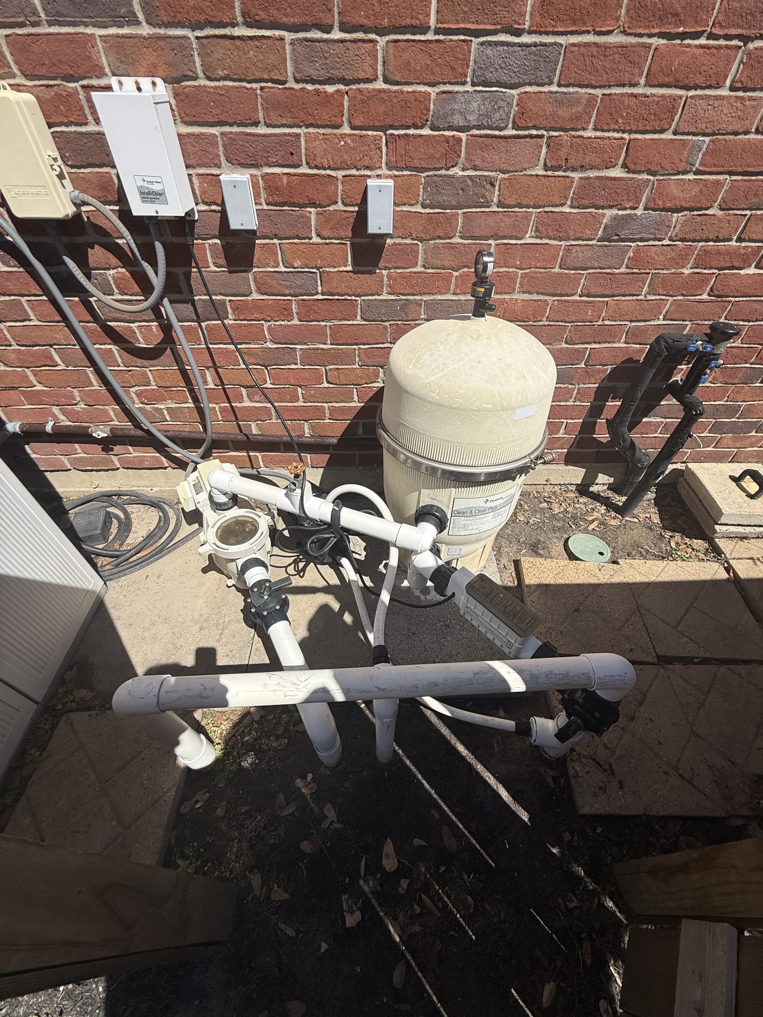 Installation of pool equipment with PVC pipes, filtration system, and electrical boxes against a brick wall.