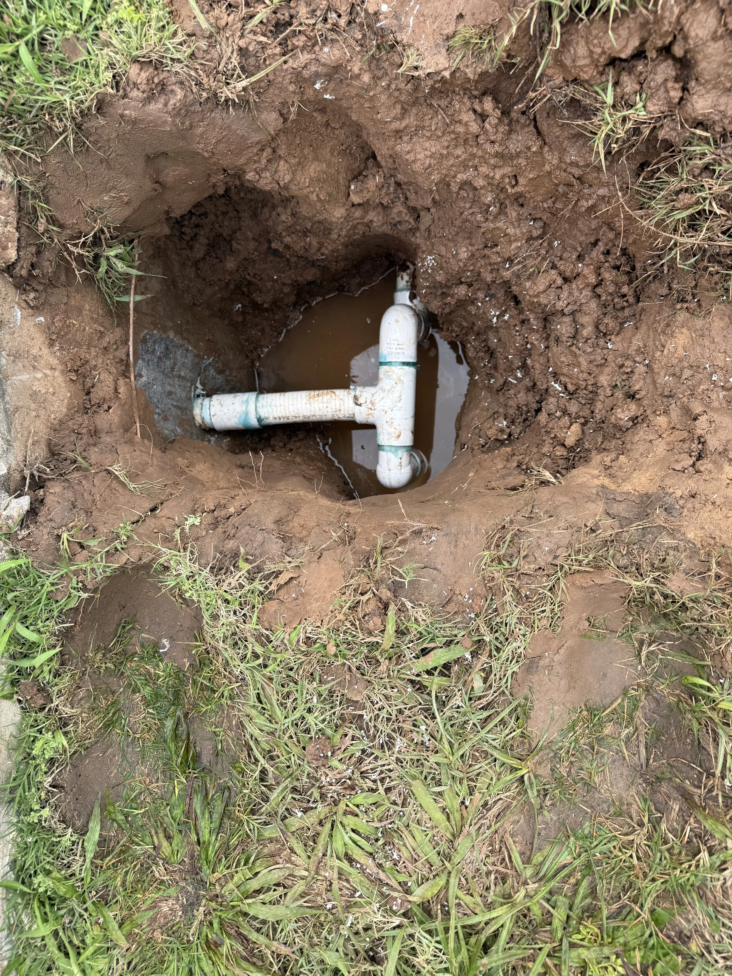 Underground pipe with water visible in a freshly dug hole in grassy soil.