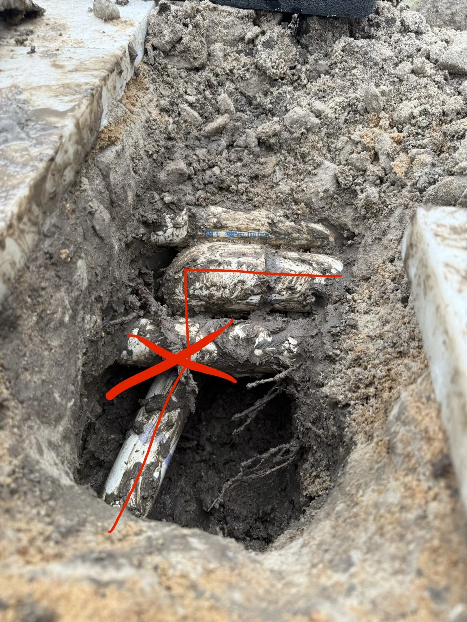 Close-up of an underground pipe or cable in a dirt trench with dirt and rocks surrounding it, marked with red annotations.
