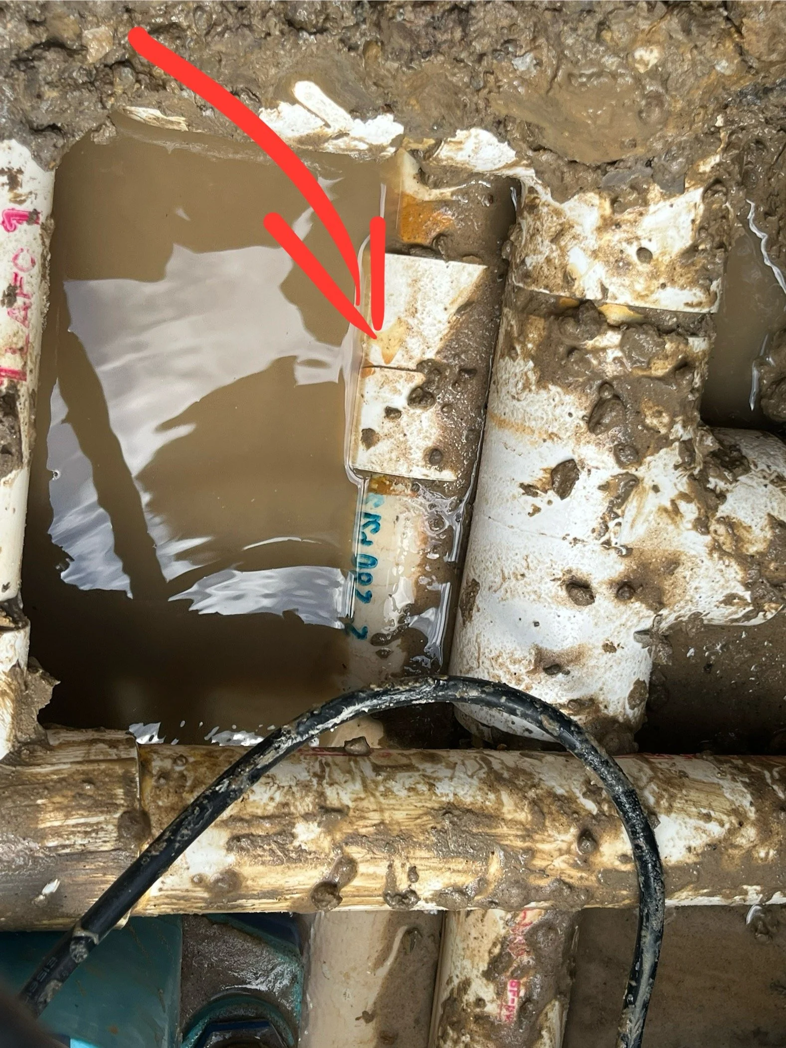 A close-up view of a plumbing issue in a bathroom or kitchen, with water leakage, muddy water in the drain, and corroded pipes.