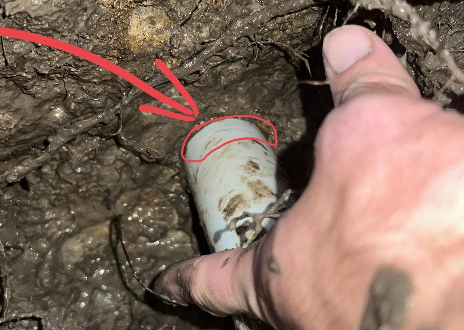Close-up of a person’s hand holding a dirty pipe in a muddy environment, with red markings and an arrow indicating a part of the pipe.