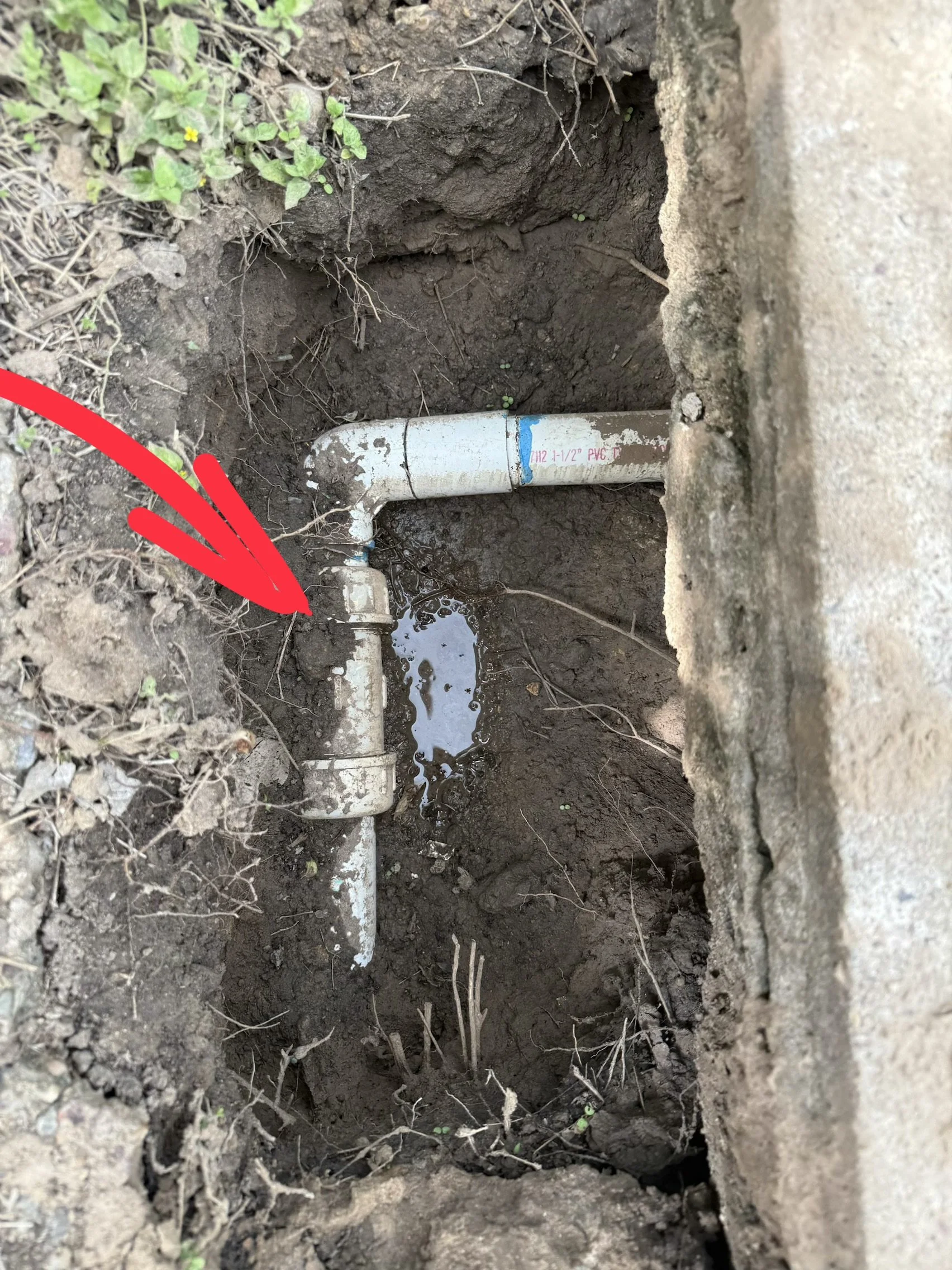 A close-up of an underground water pipe with visible leaking water, surrounded by soil and dirt.