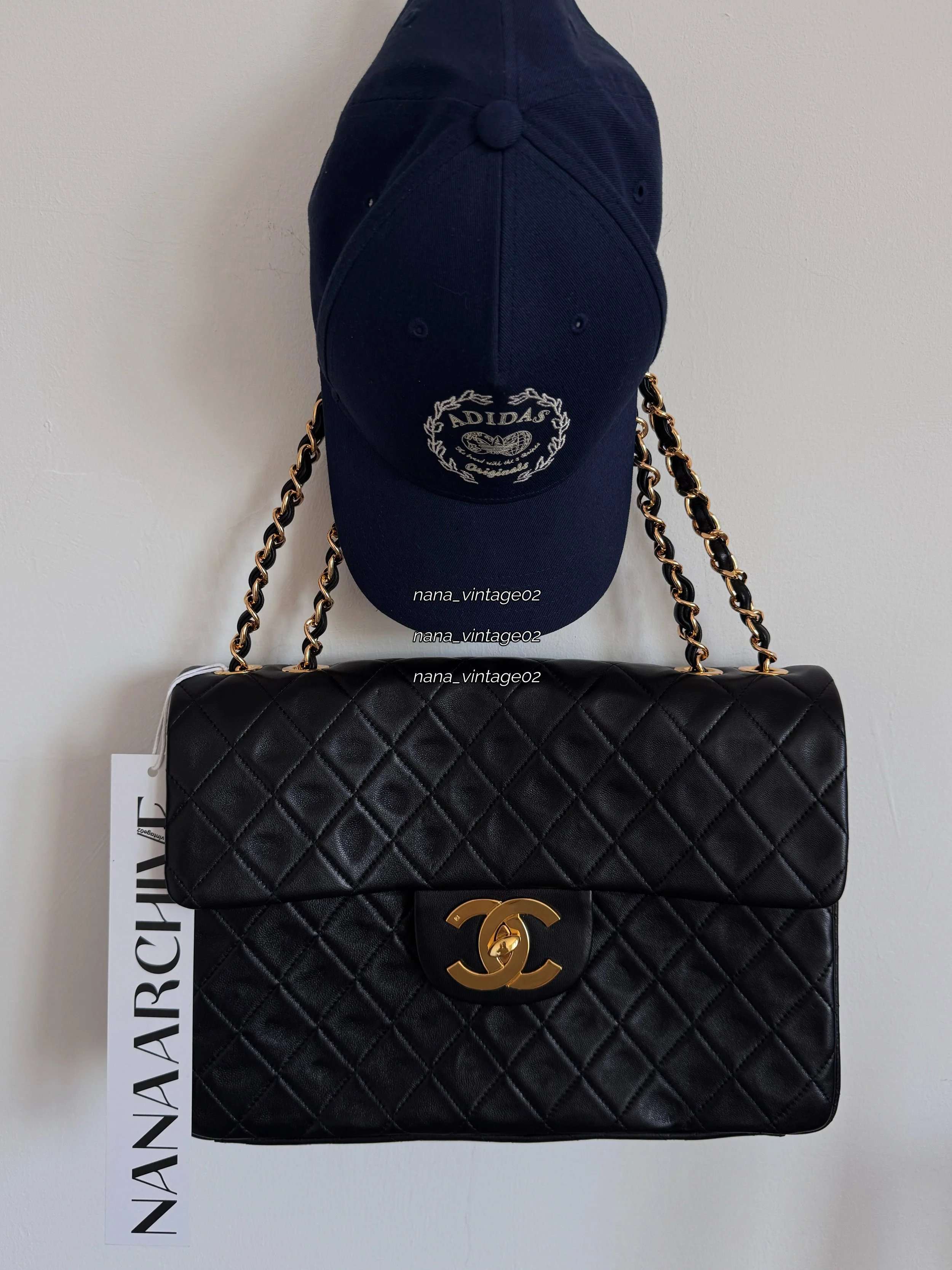 Handcrafted black quilted leather flap bag with gold chain strap displayed under an Adidas baseball cap, featuring a prominent NANAARCHIVE tag. 