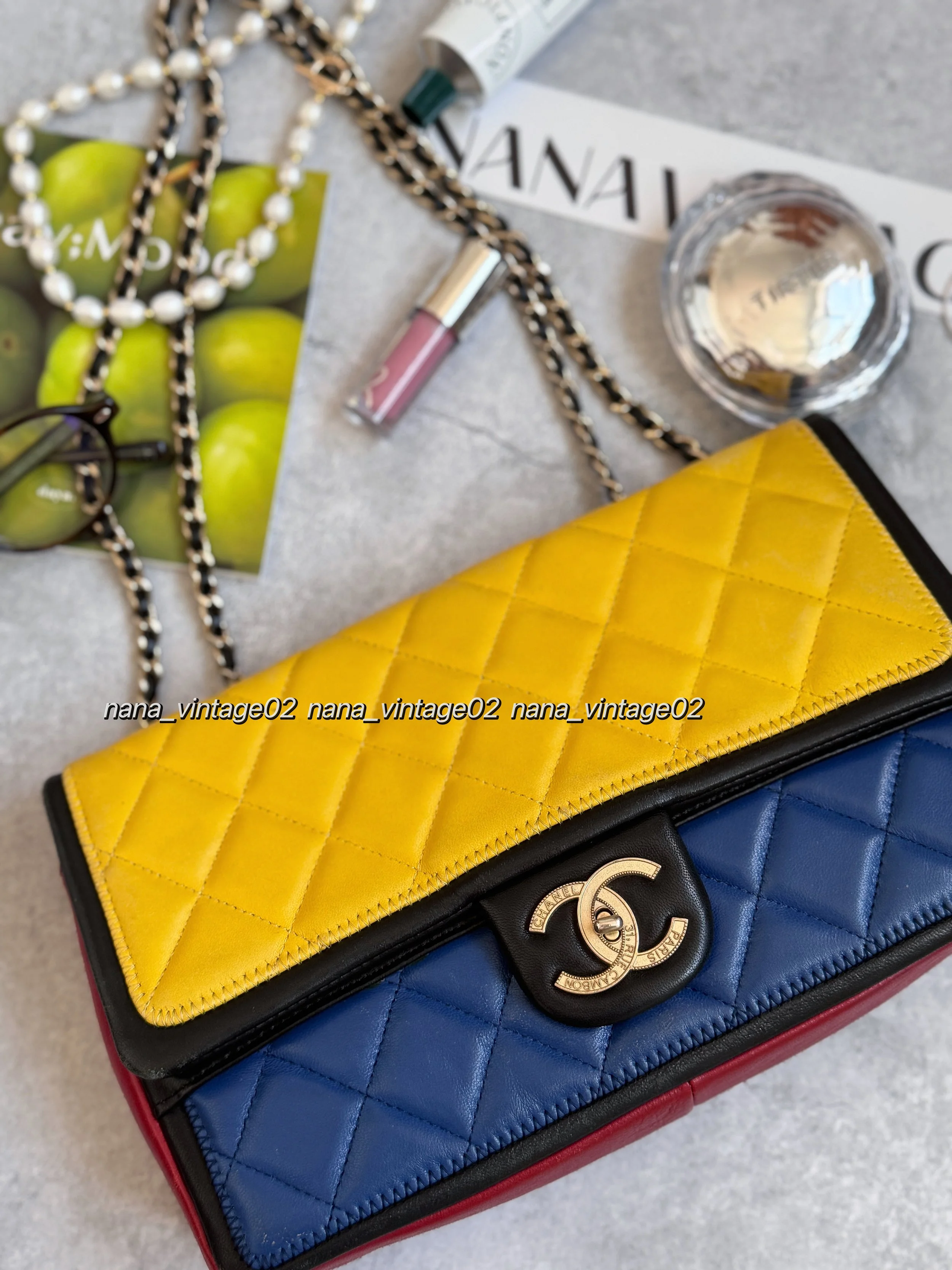 A rare Chanel vintage archive multicolor classic flap bag in yellow, blue, and red leather, displayed with a pearl necklace, cosmetics, and a store tag on a textured surface.⁠