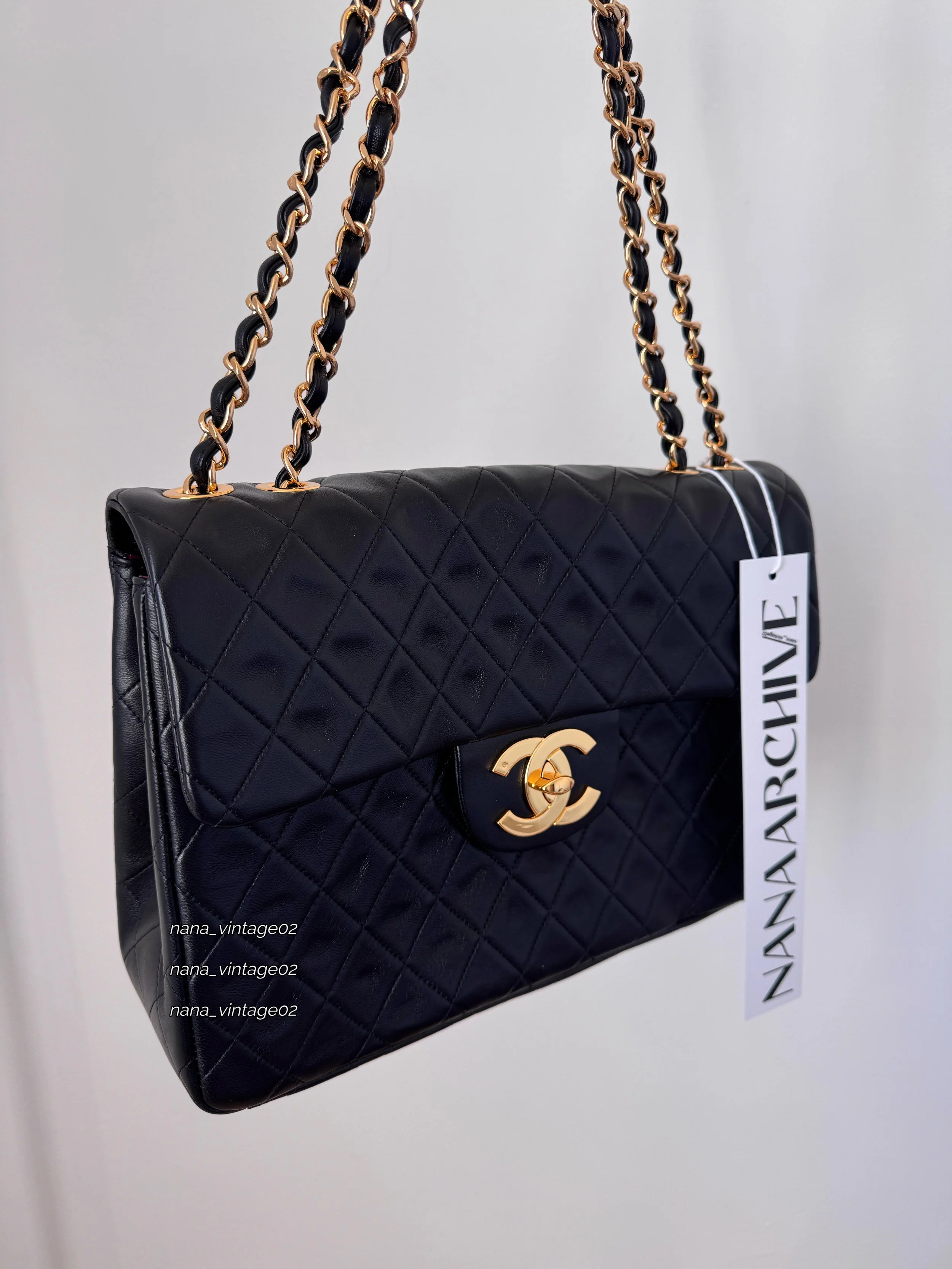 Close-up front view of the handmade black quilted flap bag with classic leather-woven chain strap and hanging brand tag against a clean background. 