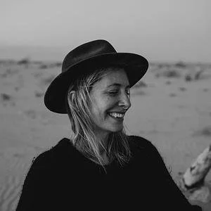 A woman smiling and wearing a hat outdoors in a desert landscape