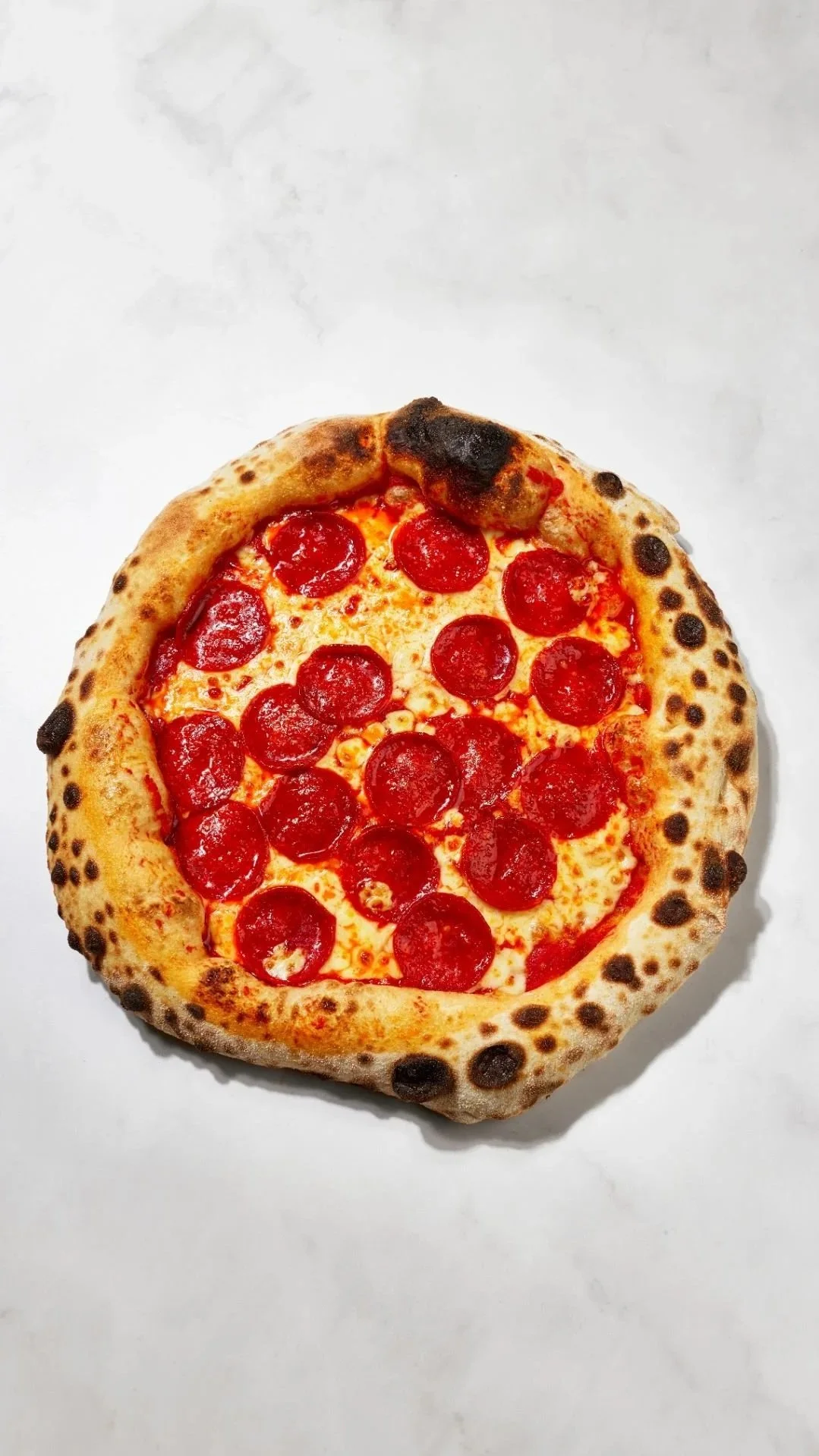 Pepperoni pizza on white surface with a nicely charred crust.