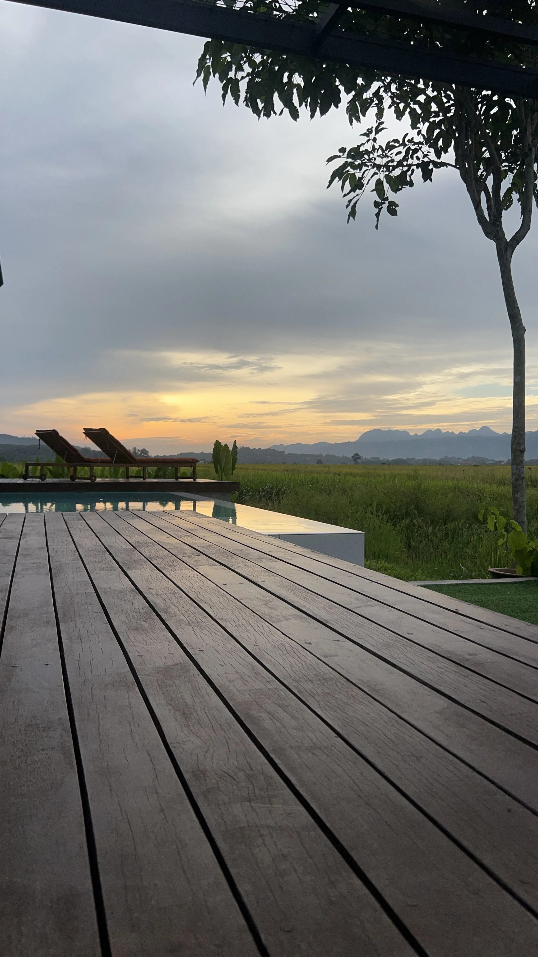 As day fades, the deck stretches toward the horizon — pool, paddy fields and the mountains become a silhouette