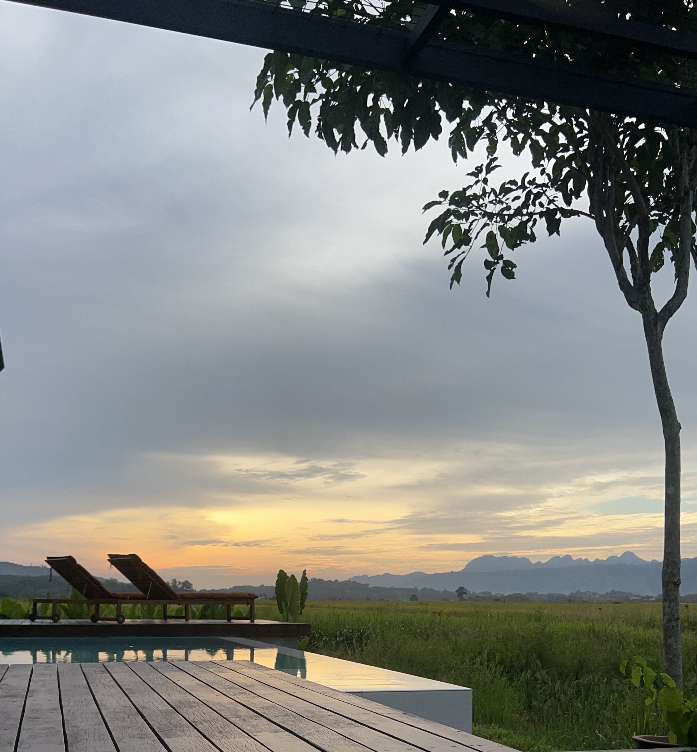 Teak pool deck leading to infinity pool at sunset with Langkawi rice fields and mountain silhouette