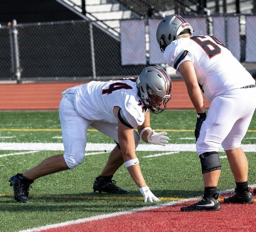 Two American football players in white uniforms and helmets preparing for a play on the field.