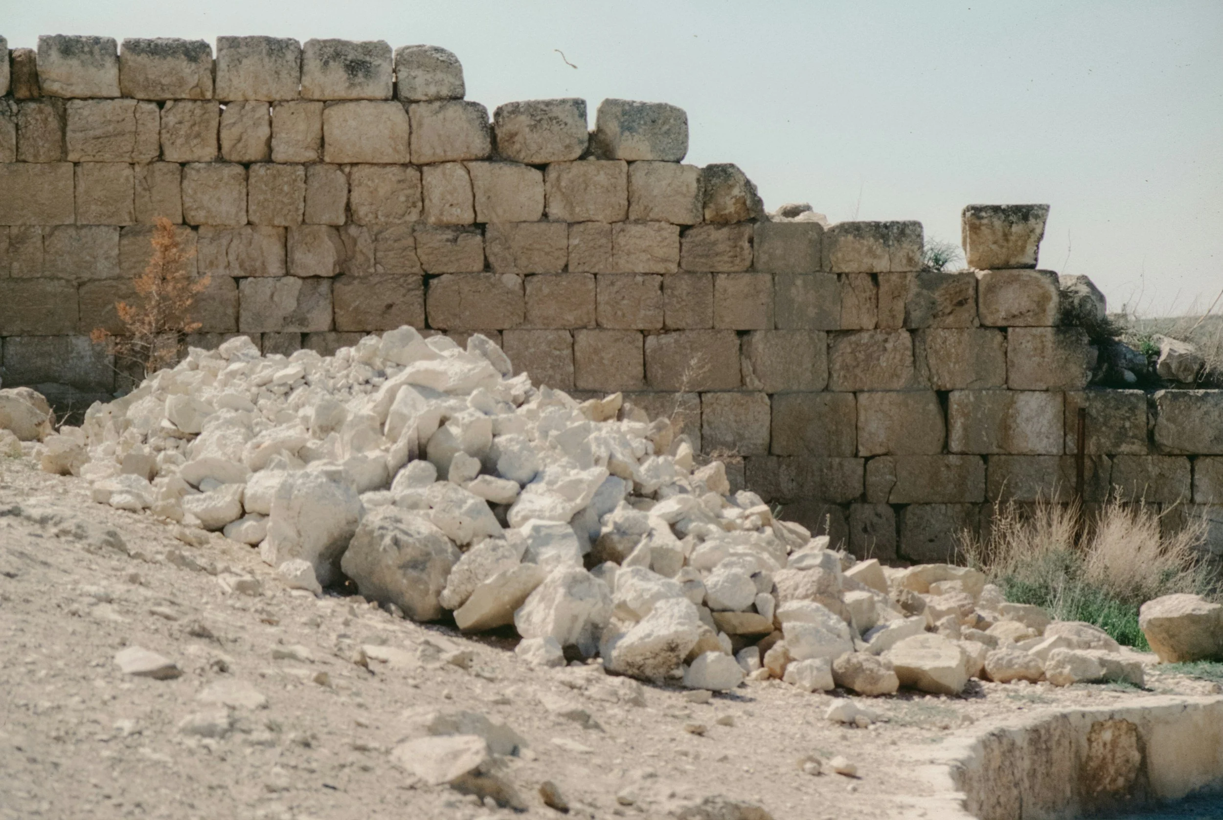 A stone wall under construction with beige rectangular stones, and a pile of white rocks and debris in the foreground.