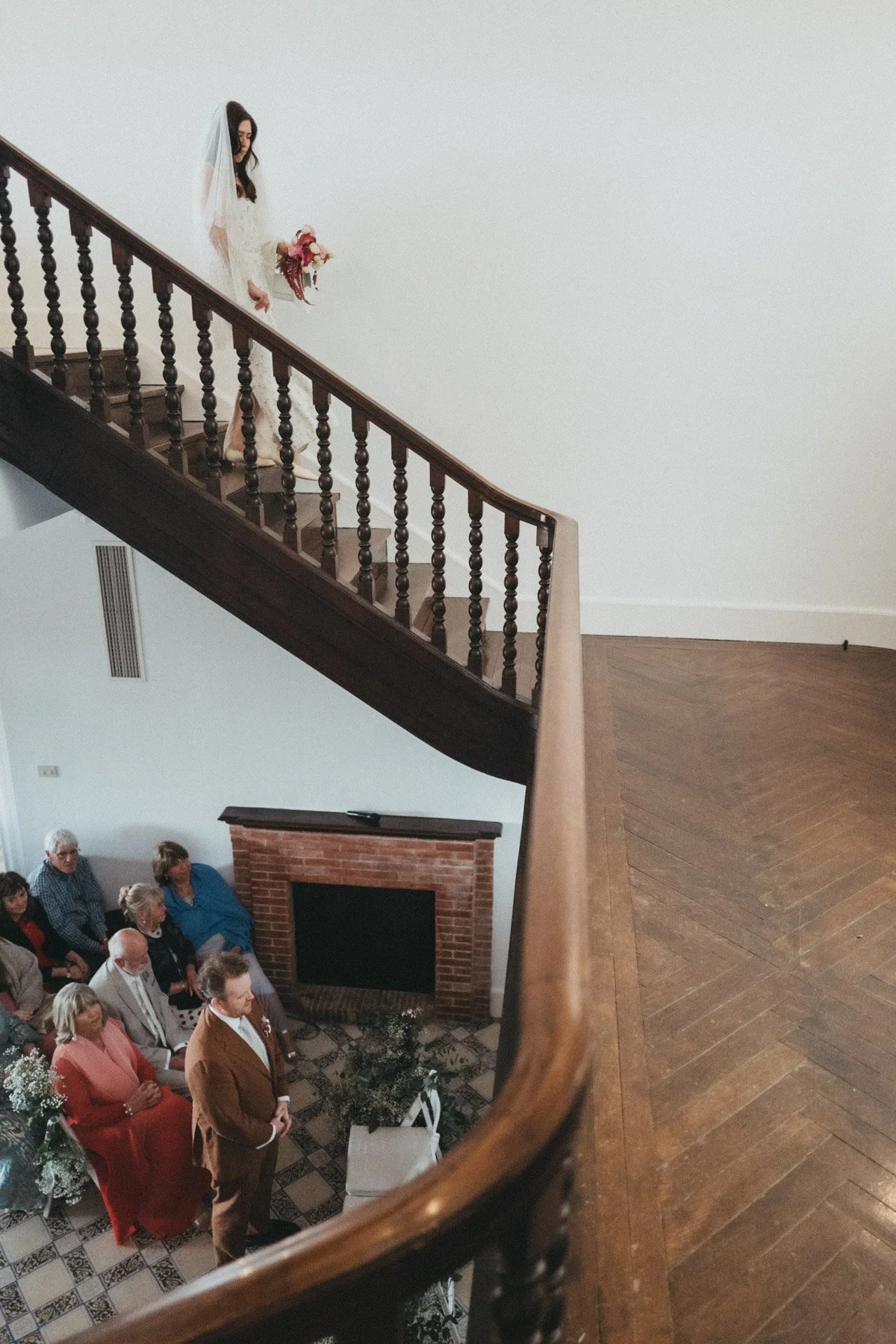 Una novia con ramo de flores bajando por una escalera de madera hacia la ceremonia en Ca l'Iborra