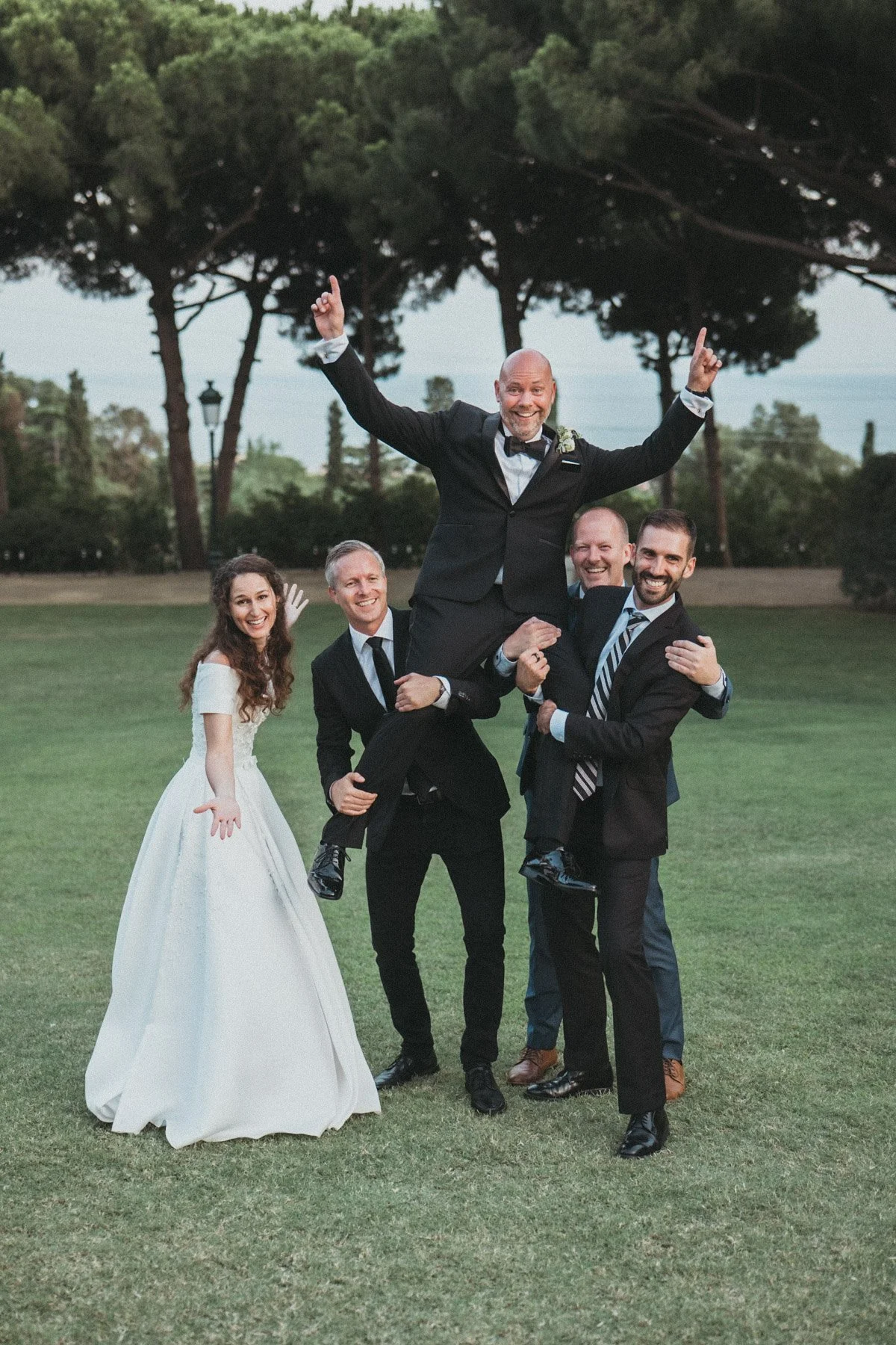Grupo de cinco personas en una boda: la novia, cuatro hombres con trajes, uno de ellos, el novio, en brazos de los otros, en Torre del Pi
