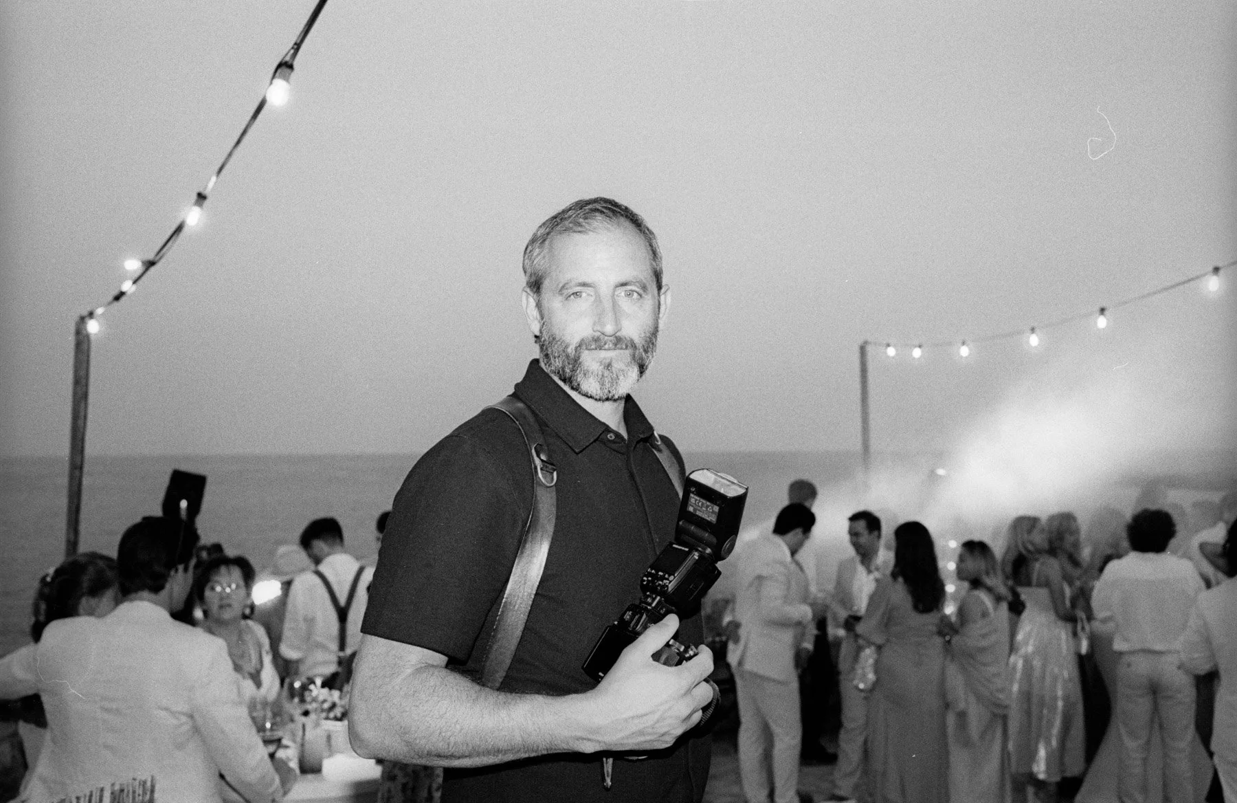 Fotógrafo de Buenafortuna sosteniendo una cámara fotográfica, en una boda al aire libre con luces y muchas personas en el fondo