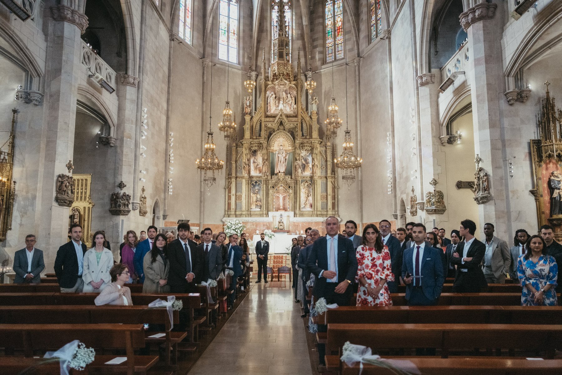 Grupo de personas vestidas formadamente dentro de una iglesia, frente al altar decorado con figuras religiosas y candelabros, durante una ceremonia o evento especial.