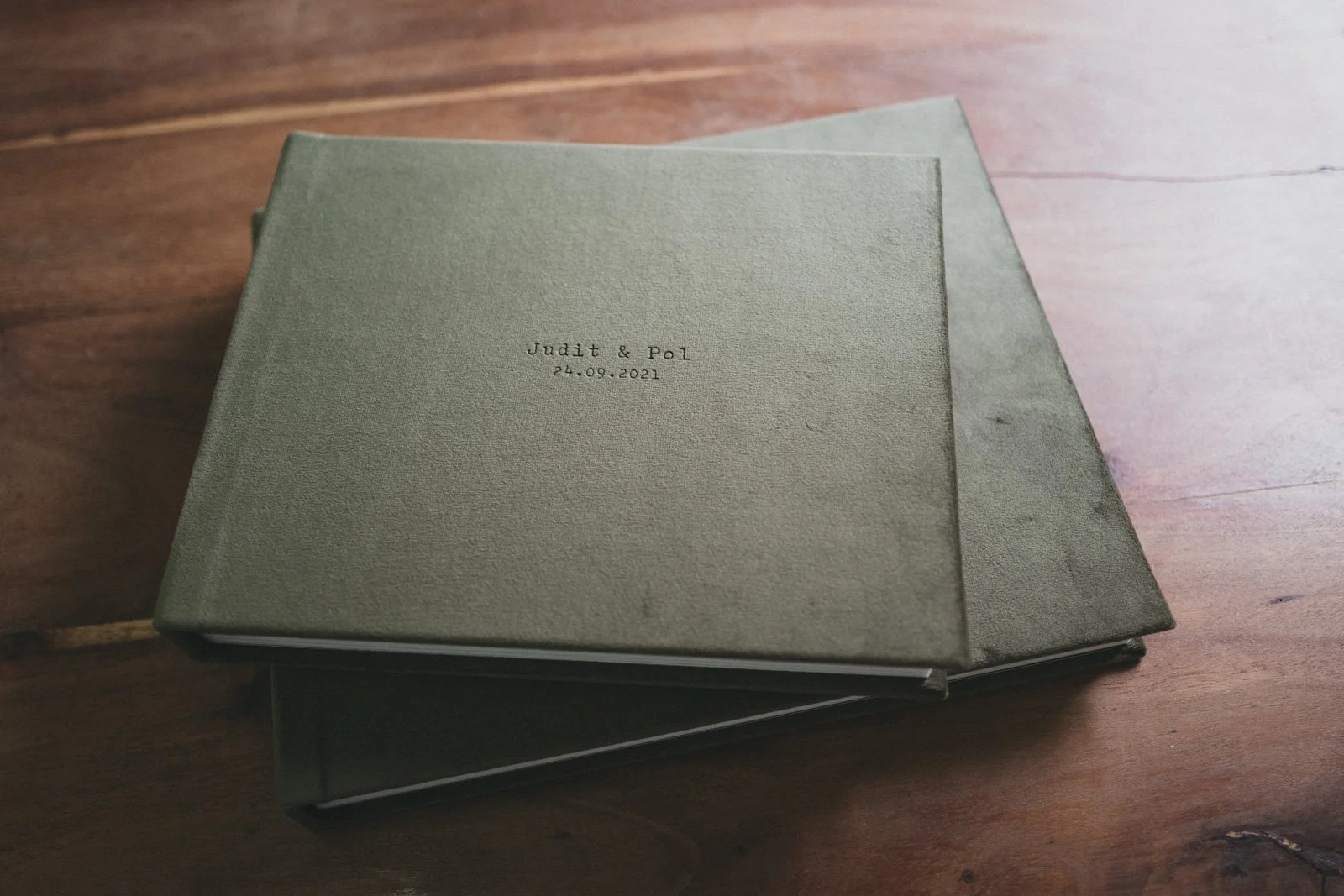 Álbum de boda de Buenafortuna con tapa verde y texto en una mesa de madera. A Buenafortuna wedding album with a green cover and embossed text, displayed on a wooden table.