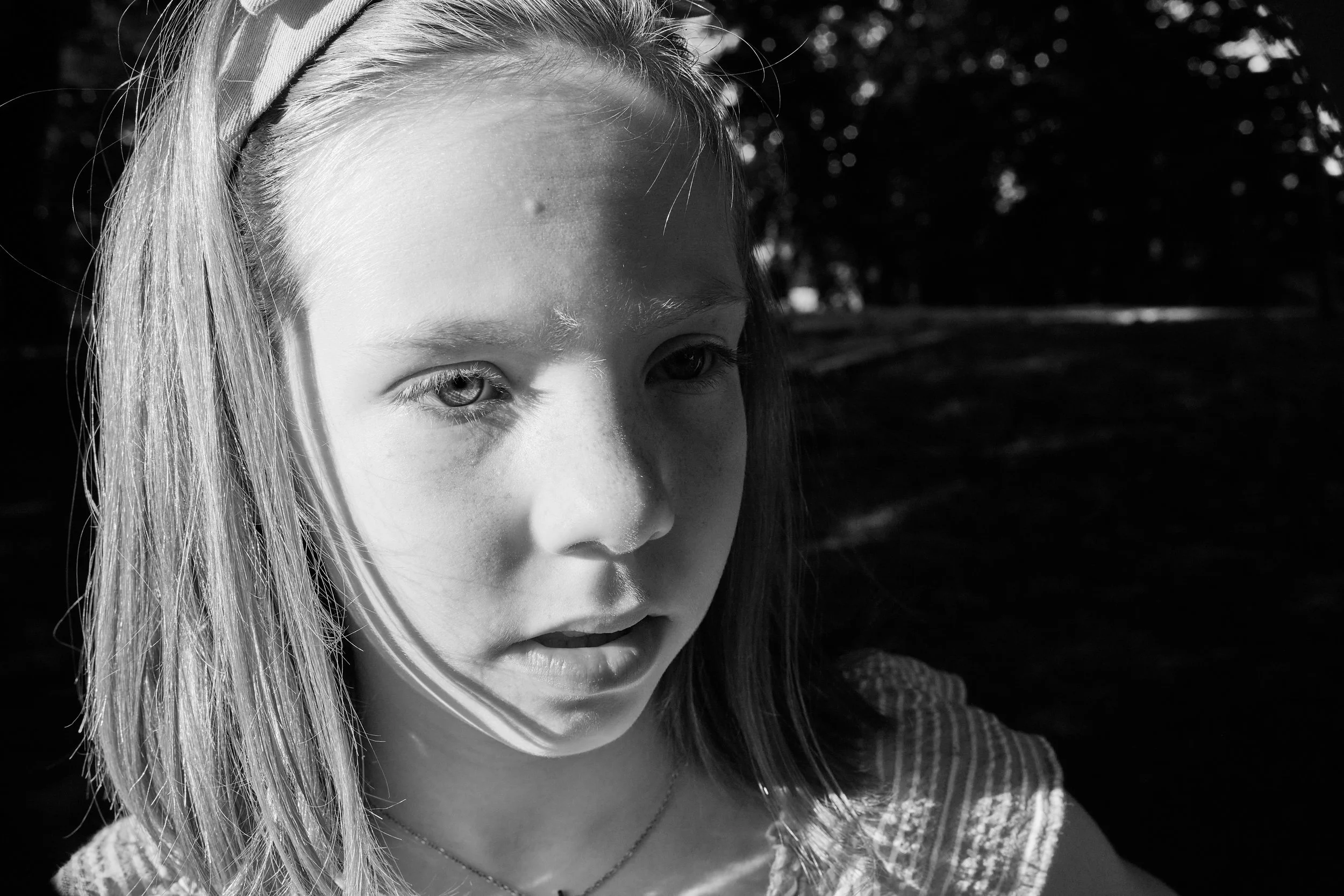 Karakterni portret deklice, resen pogled, lasje skozi svetlobo. Iz serije „Karakter“ — dve plati ene osebe. Črno-bela uredniška fotografija. Maja Ratajc.
