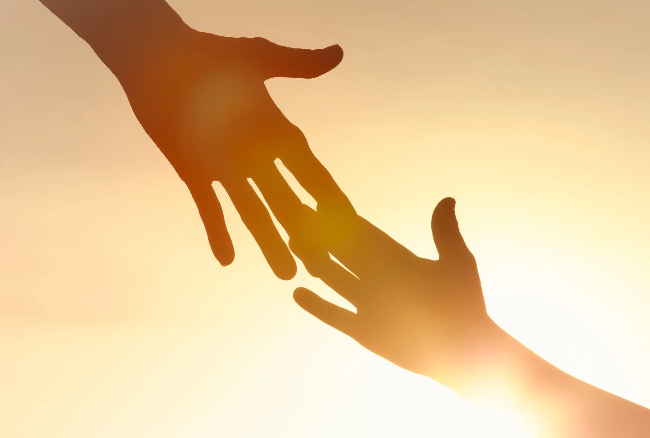 Silhouette of two hands reaching towards each other against a sunset sky.