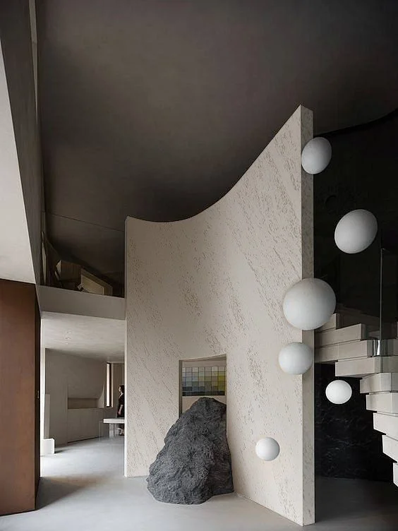 Modern interior with a large rock, abstract white sphere light fixtures, and a curved textured wall.