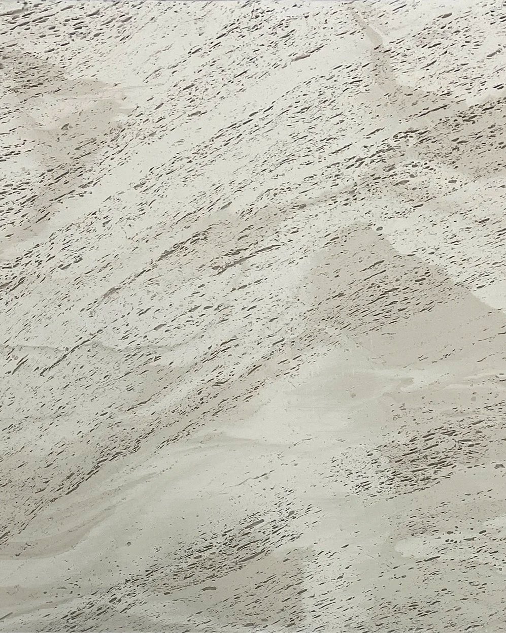 Close-up of a light-colored, textured surface with fine, dark streaks and rough patches.