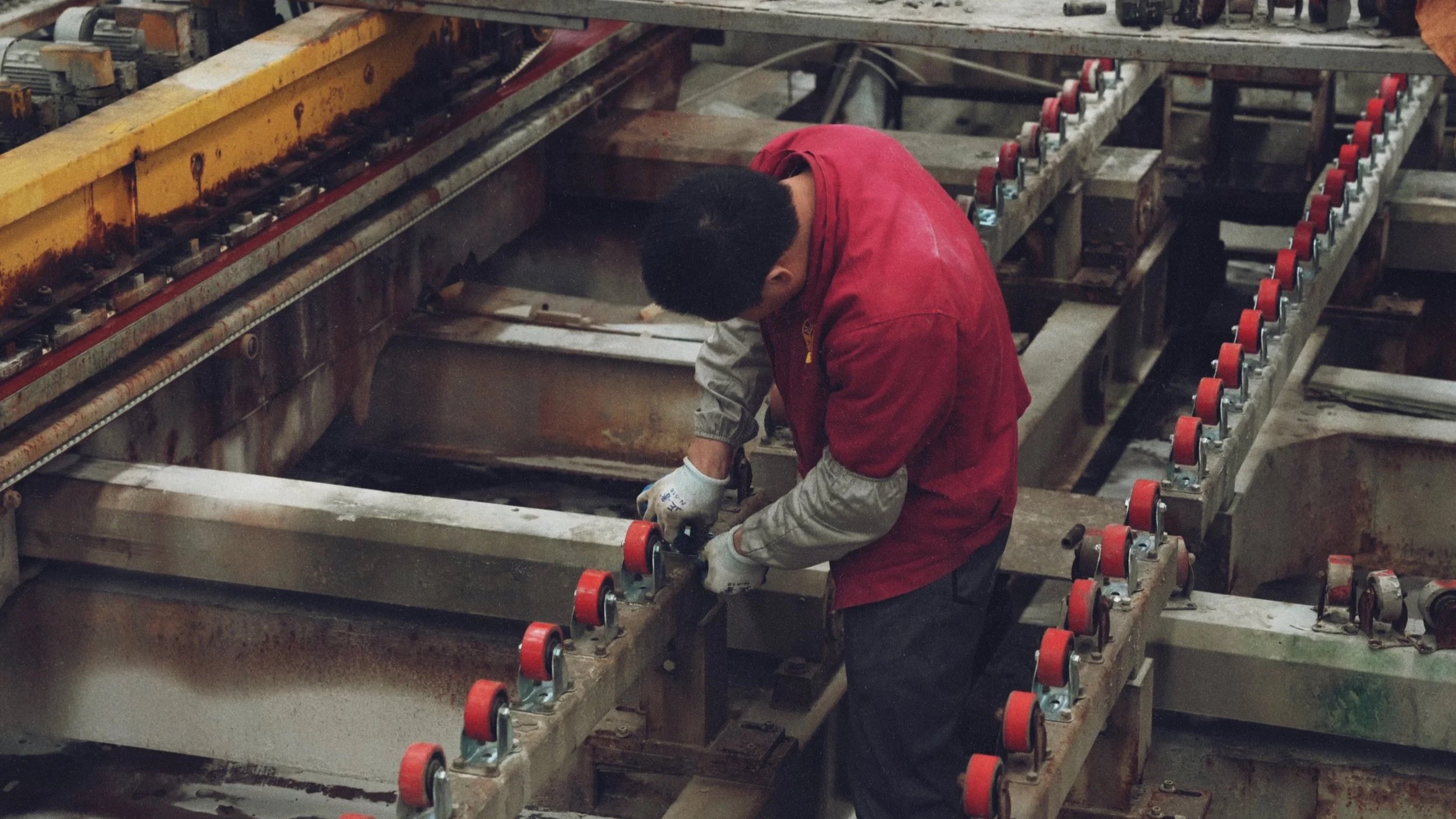 A worker in a red jacket using tools on large industrial machinery in a factory or workshop.