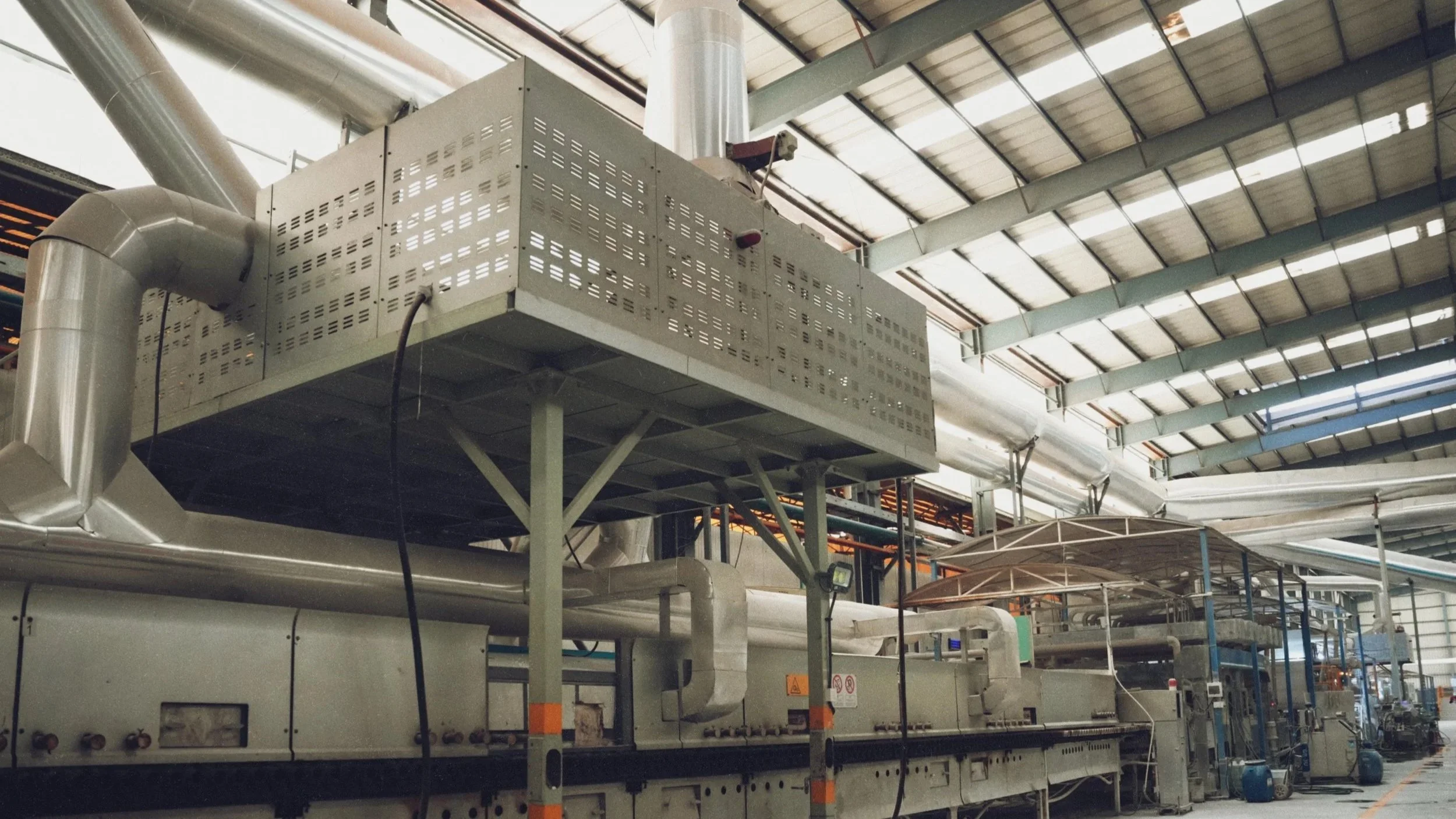 Industrial facility with large machinery and ducts inside a warehouse with a high, curved metal roof.