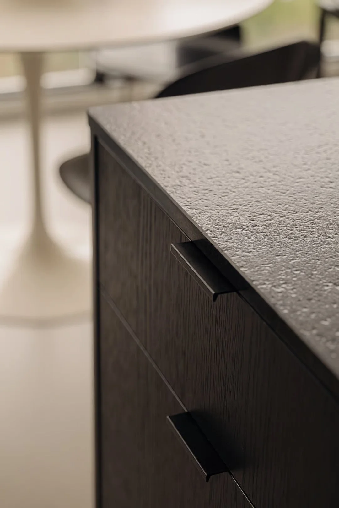 Close-up of a textured black cabinet with black handles in a modern kitchen or office space.