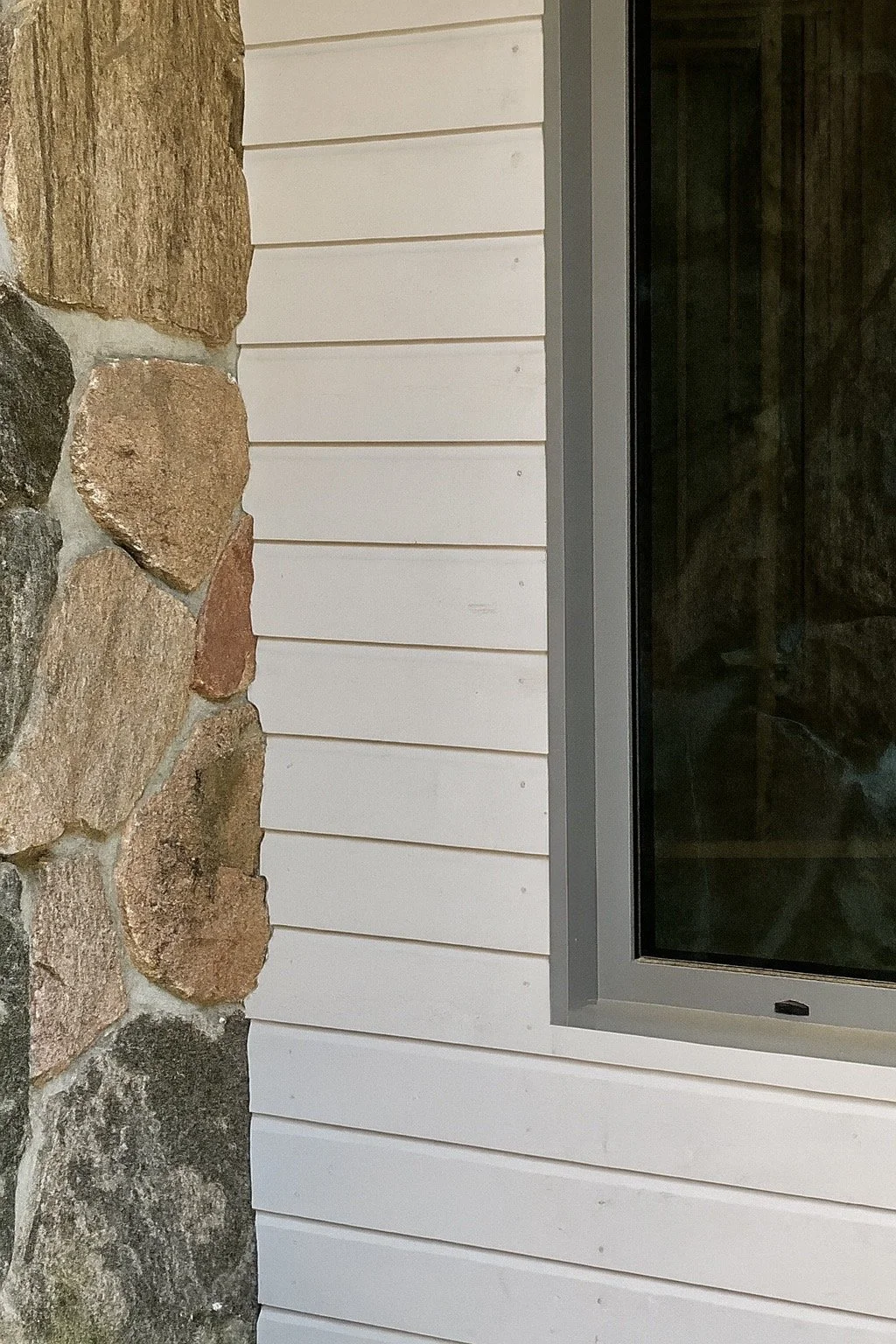 Part of a building exterior showing stone wall, white siding, and window.