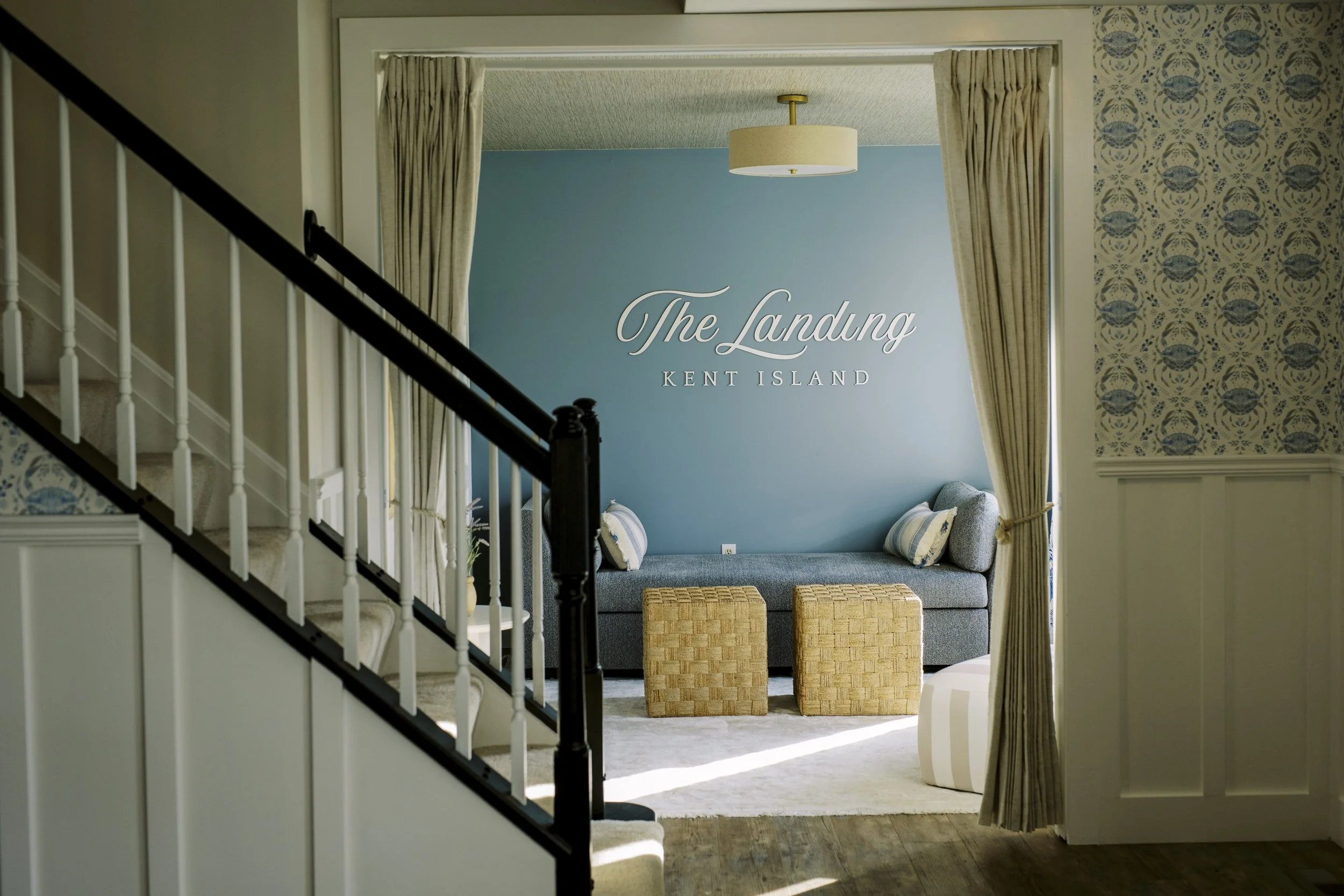 Interior of a hotel room or suite with a lounge area, featuring a blue accent wall, a chandelier, curtains, a sitting bench, and decorative pillows.
