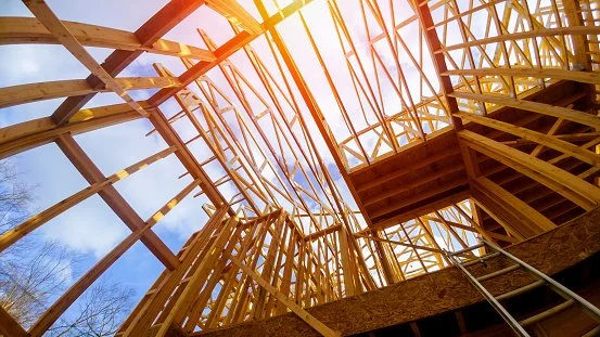 Wooden framing structure of a building under construction with sunlight shining through.