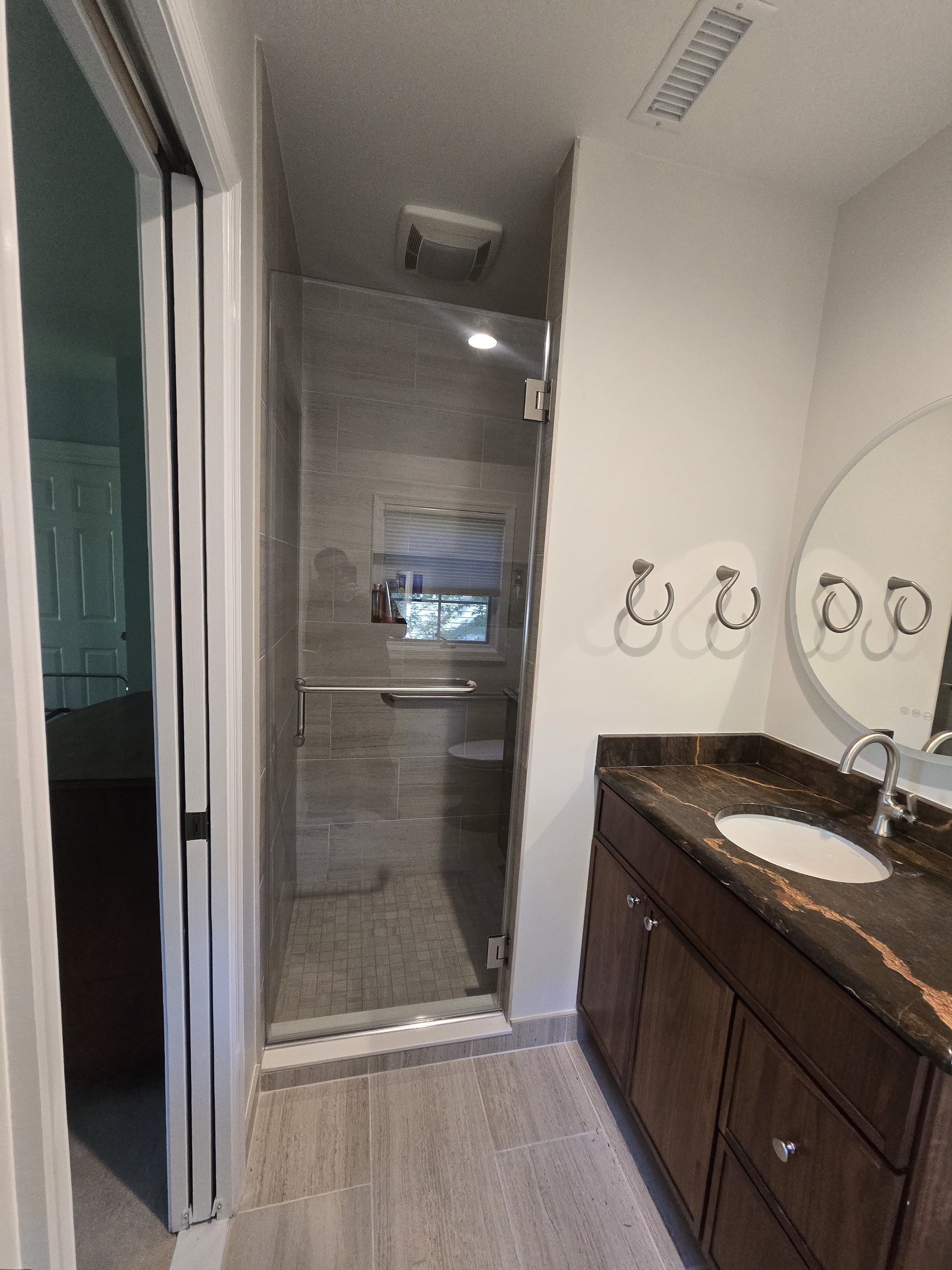 Bathroom with a shower stall, a sink with a dark marble countertop, a mirror, and three towel hooks on the wall.