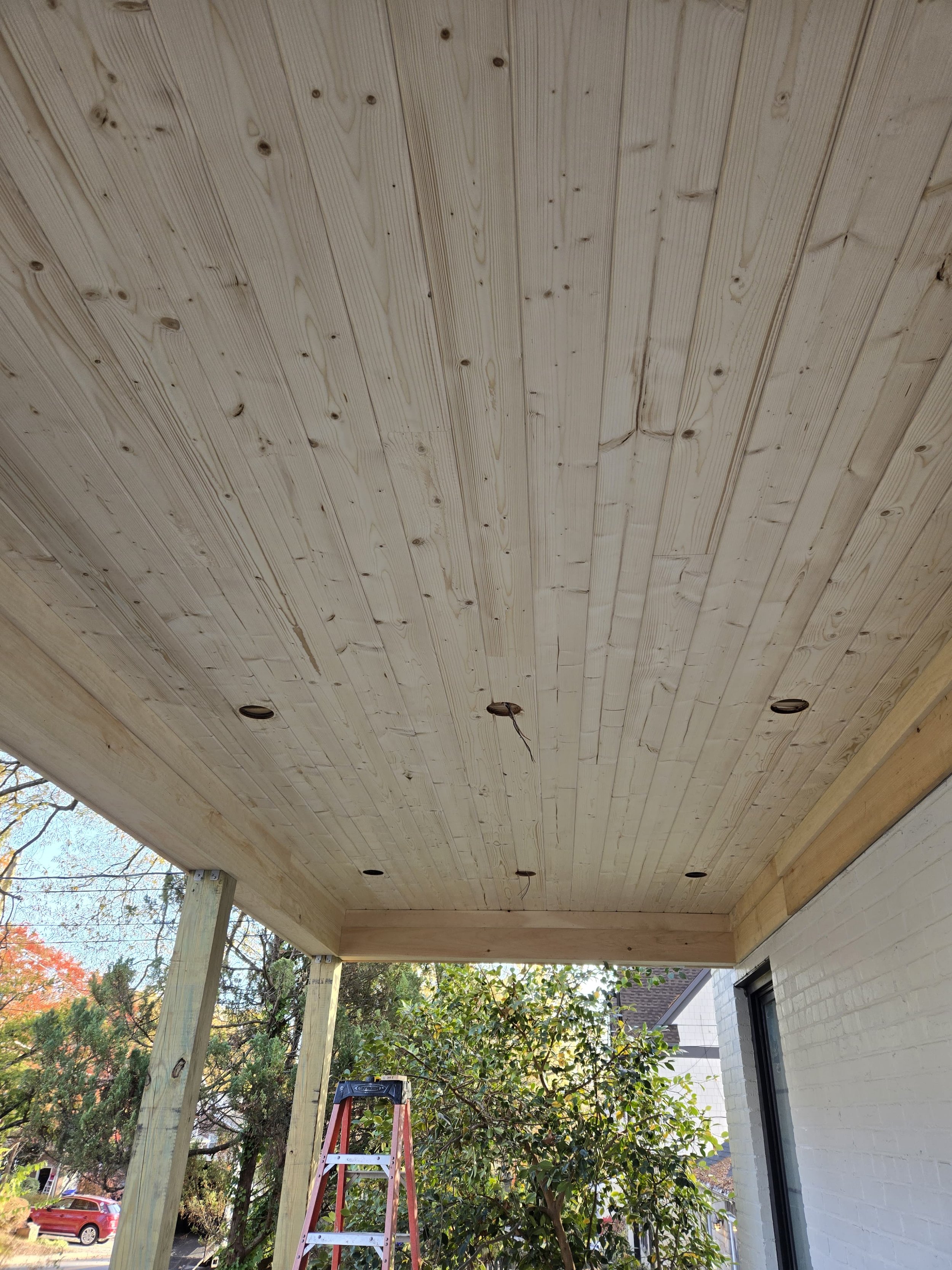 Under construction porch ceiling with recessed lighting, surrounded by trees and residential neighborhood